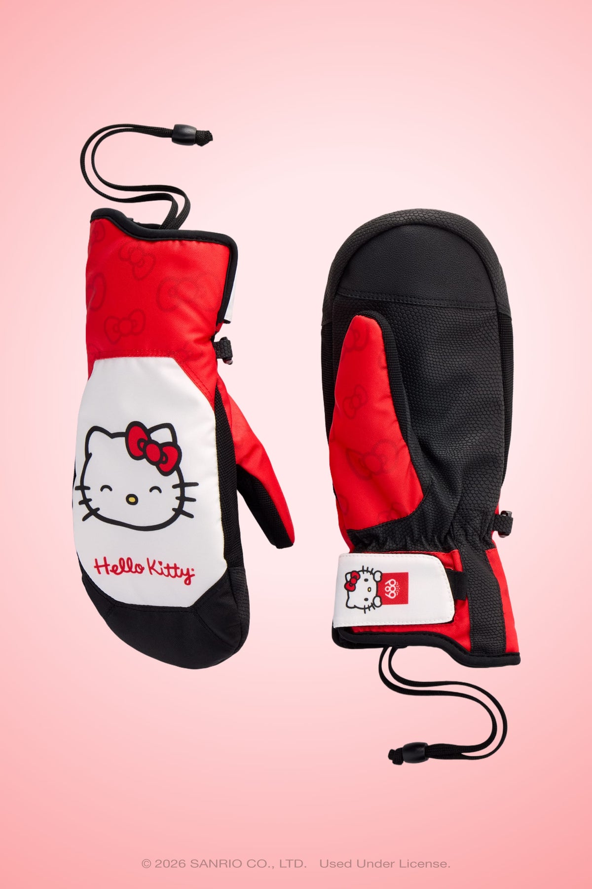 Two 686 Women’s Revel Mitts in red, black, and white—featuring Hello Kitty’s face, a red bow, and “Hello Kitty” text—are displayed on a pink gradient background. Each mitten includes a black wrist strap.