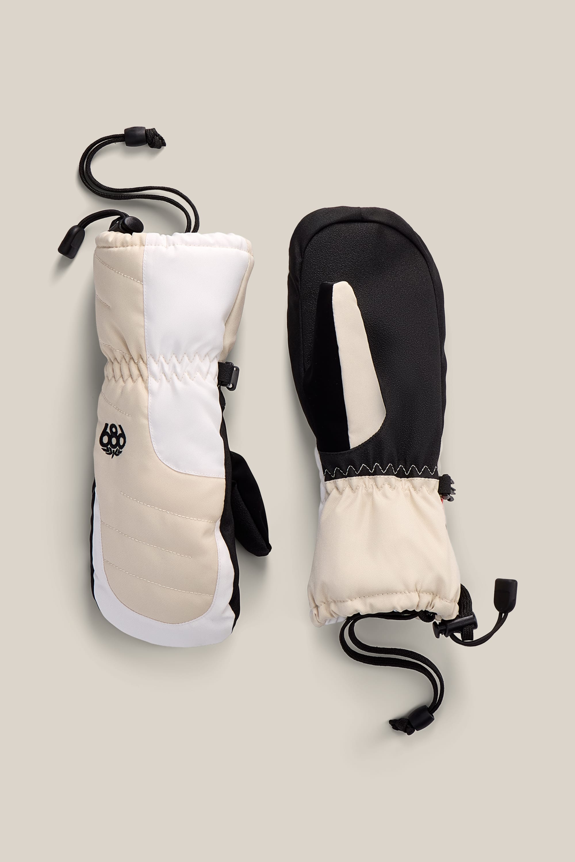 The 686 Youth Heat Insulated Mitt by 686 is featured in beige, white, and black, displayed from both the palm and back sides on a neutral background. Equipped with adjustable wrist cords, these stylish poly mitts are designed for durability and comfort—ideal for winter adventures.
