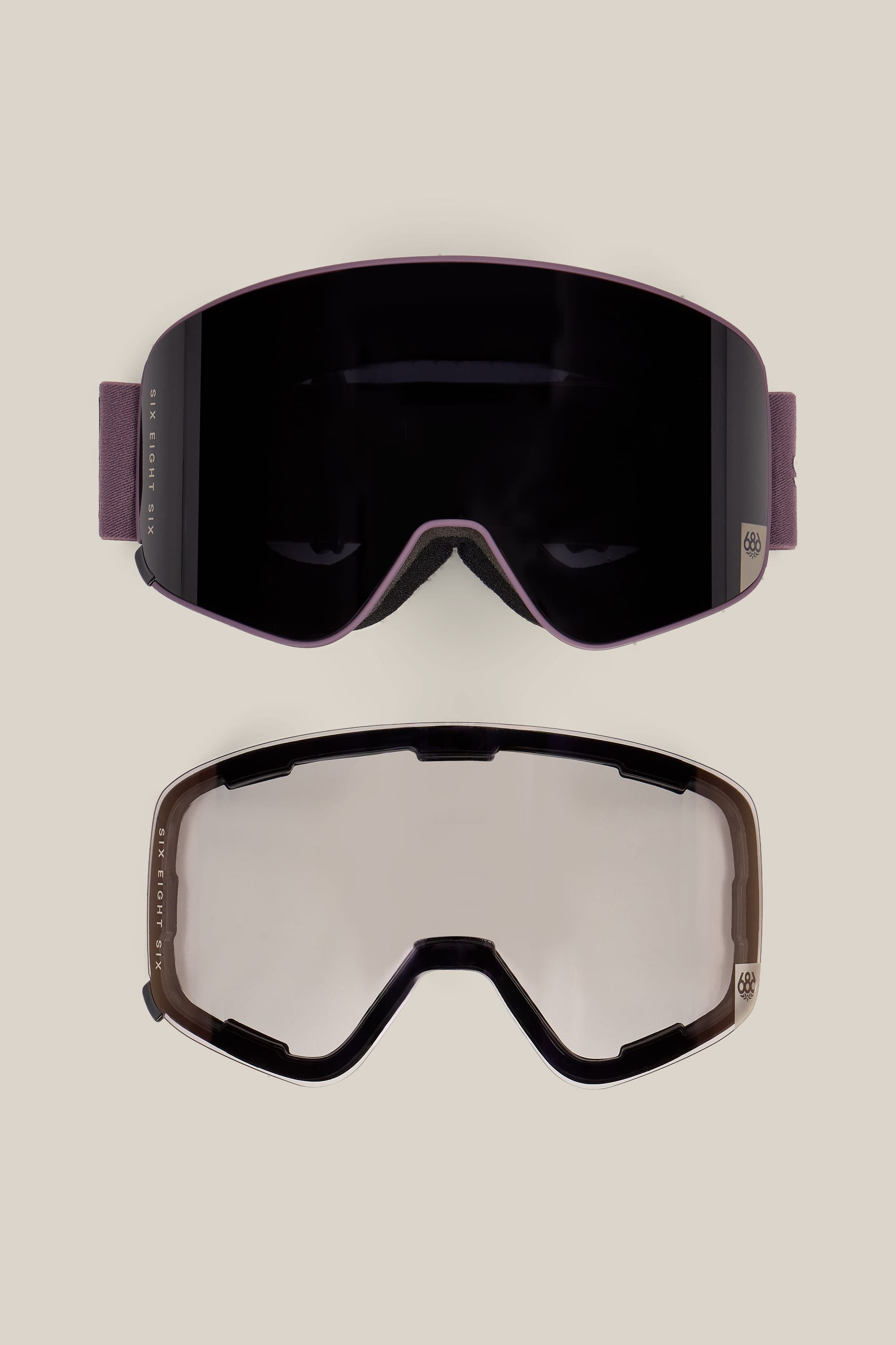 Two 686 SMARTY® Magnetic Goggles by 686 are shown on a light background: one featuring a dark lens with a purple strap, and the other showcasing a clear lens with a black frame. Both models highlight a sleek, modern design.