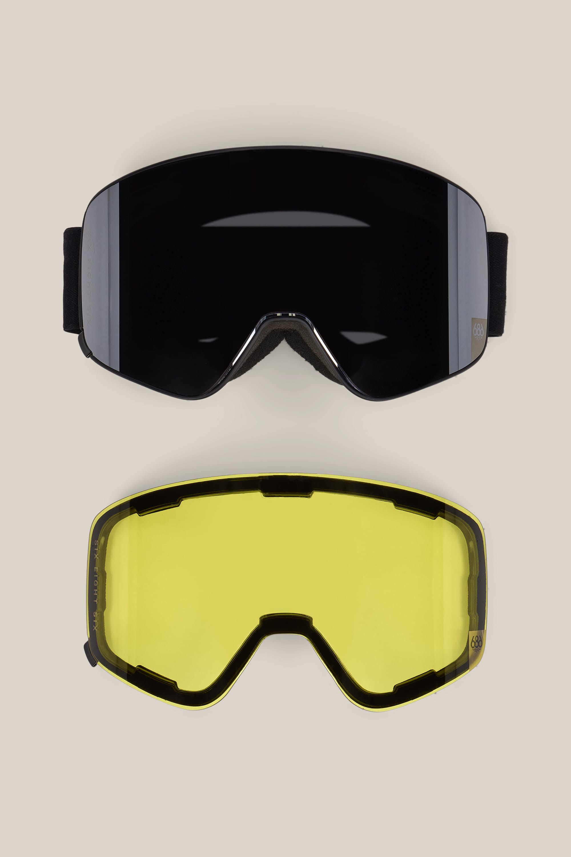 Two interchangeable 686 SMARTY® Magnetic Goggle lenses by 686, one dark-tinted and one yellow-tinted, are displayed on a neutral background. Each lens features a black frame with a small logo on the side.