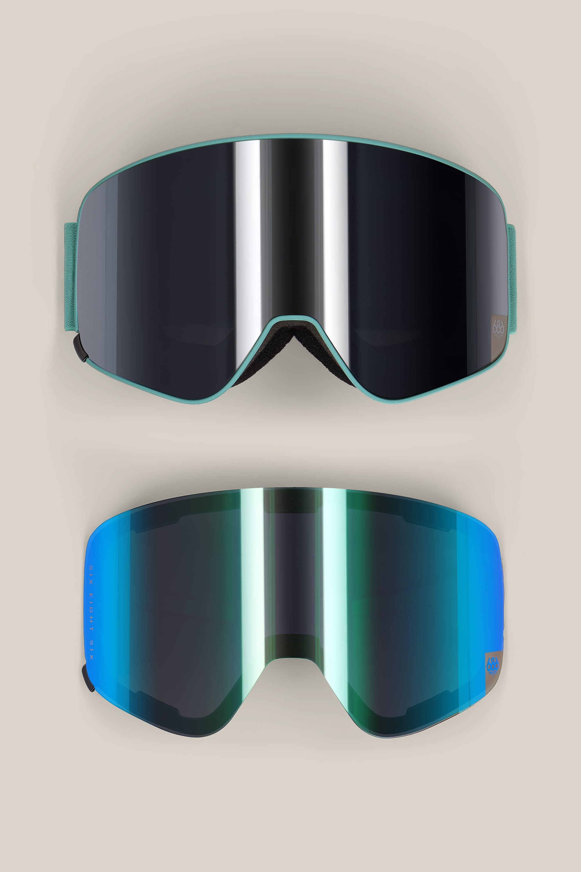 Two 686 SMARTY® Magnetic Goggles by 686—one featuring a black reflective lens and the other a blue-green reflective lens—are displayed on a light beige background.