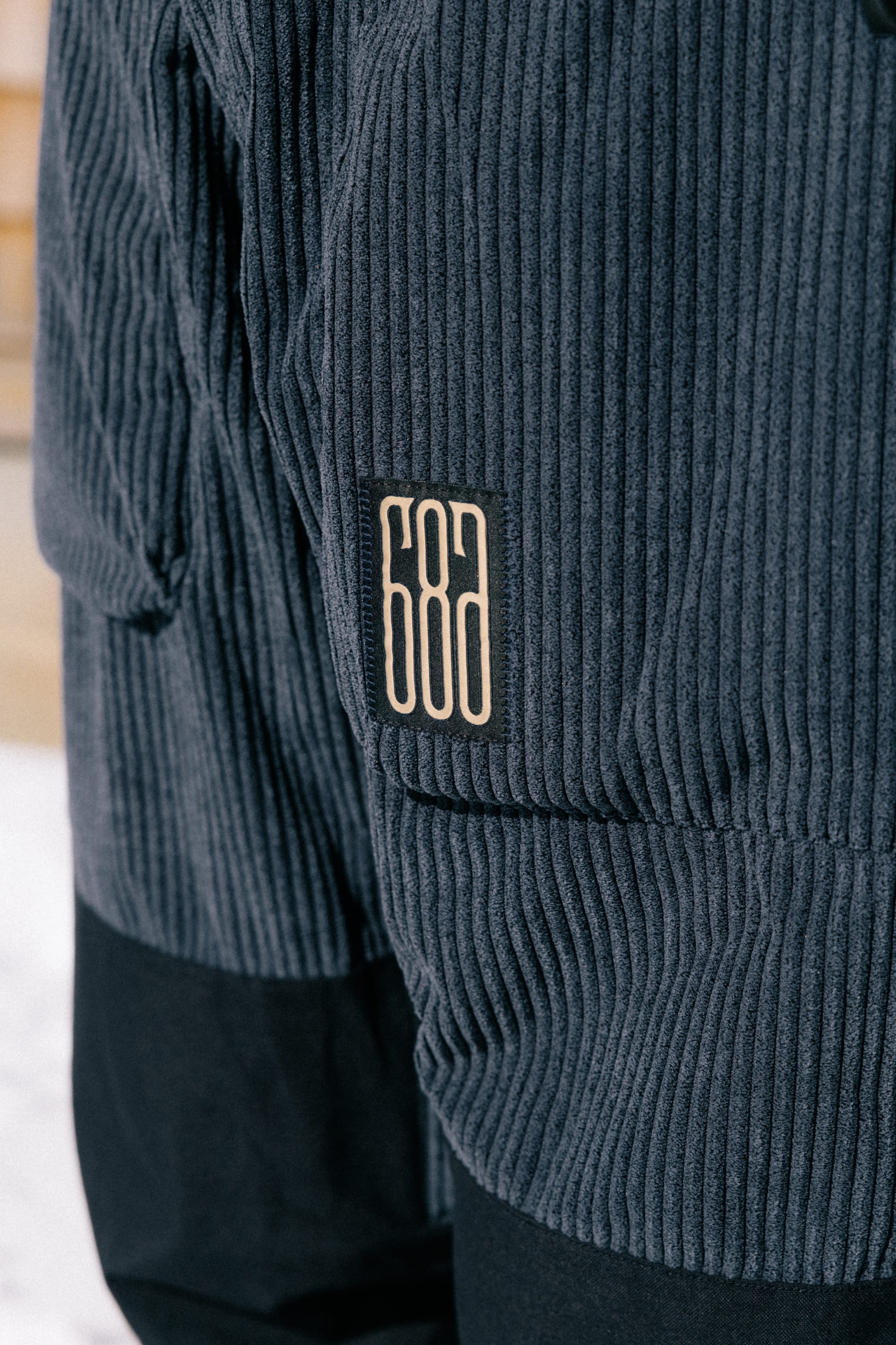 Close-up of a dark gray 686 Ghost™ 2.5L Pant featuring a stitched rectangular patch with the number 686 in white, positioned on the side.