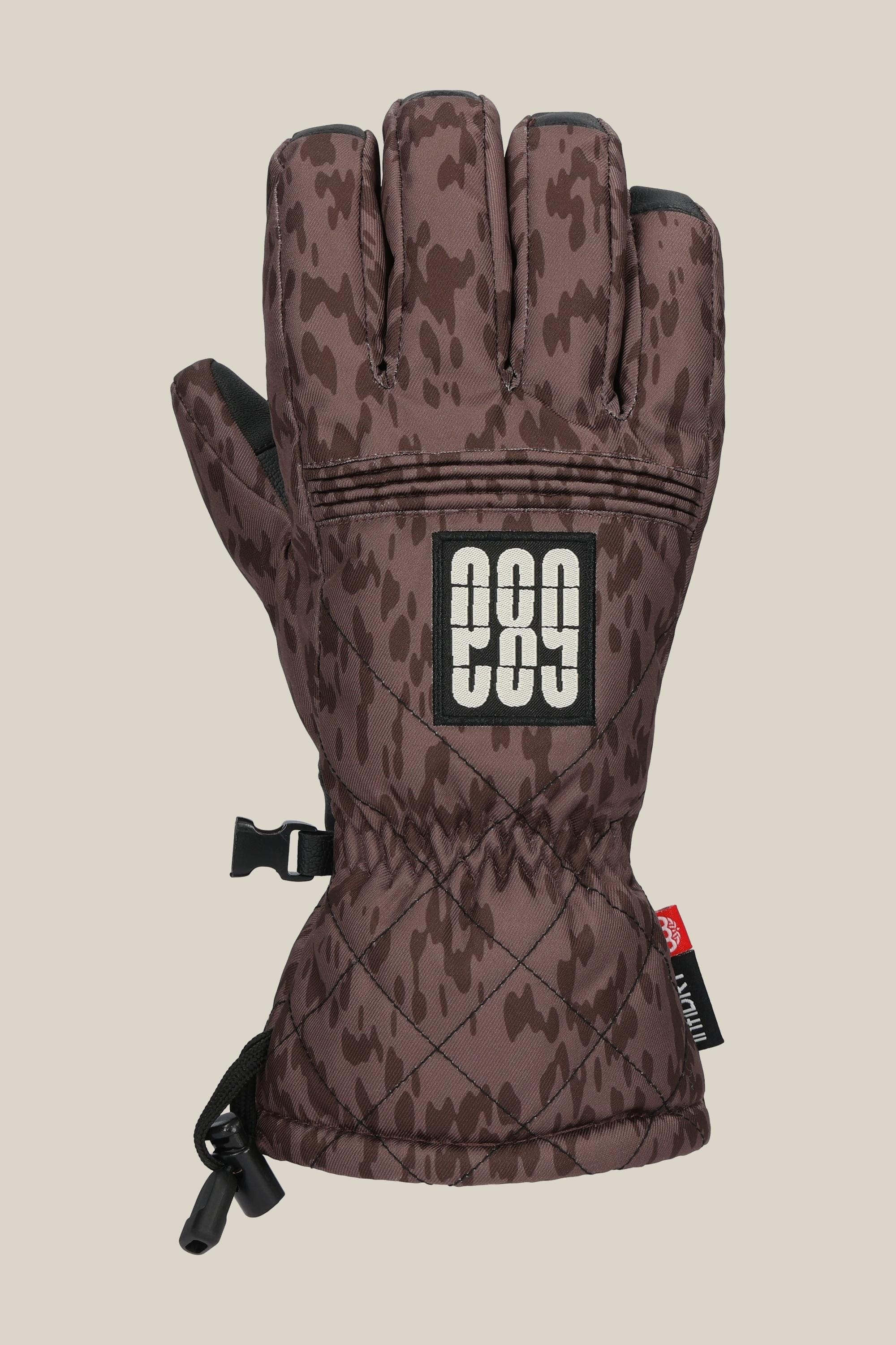The 686 Womens Jubilee Glove features a brown camouflage PU exterior, a black and white 686 logo patch on the back, an adjustable wrist strap, and a drawstring cuff closure.