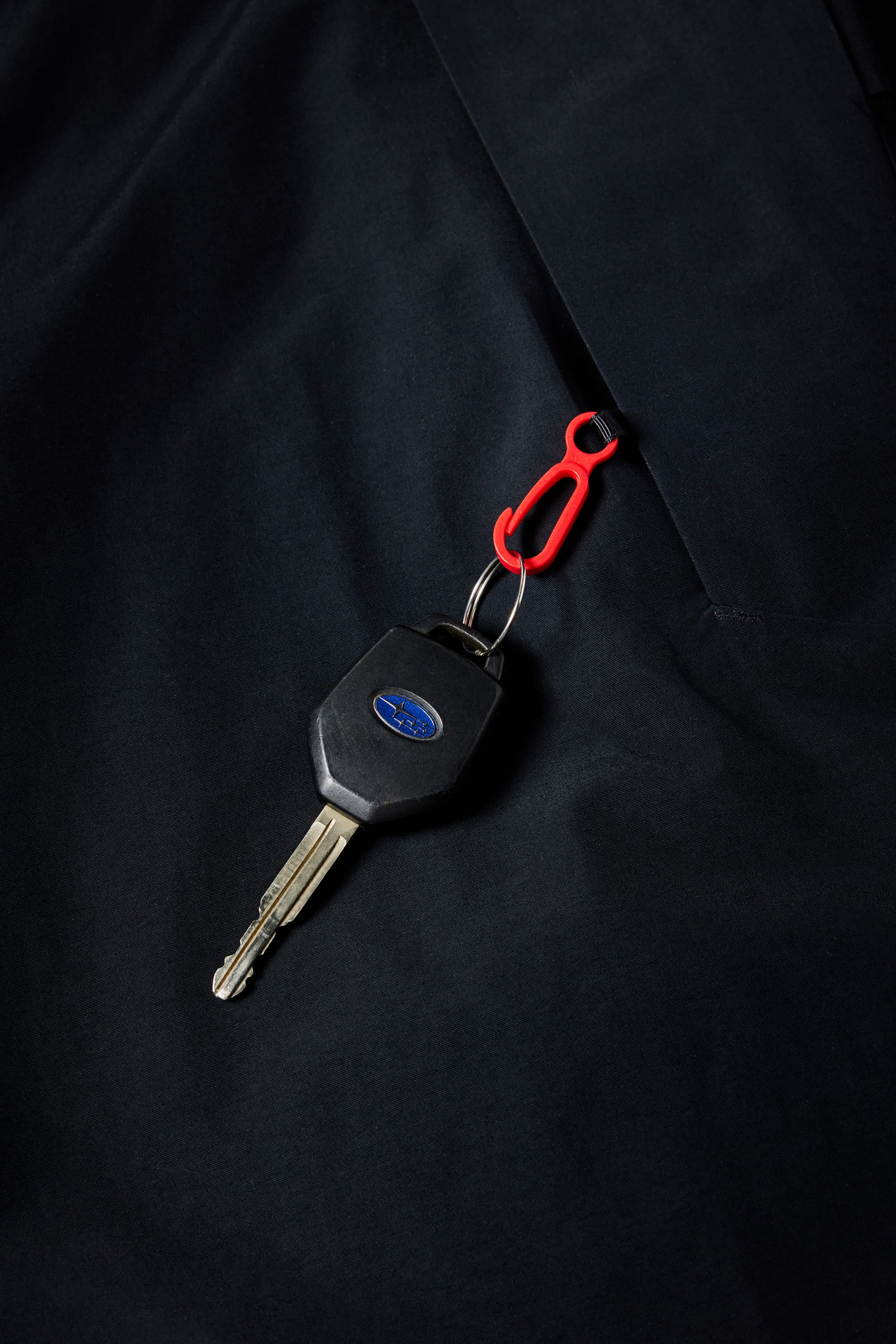 A car key with a black plastic head and blue oval logo is attached to a red plastic key clip, resting on the fleece-lined sleeve of the 686 Youth Waterproof Hoody by 686.