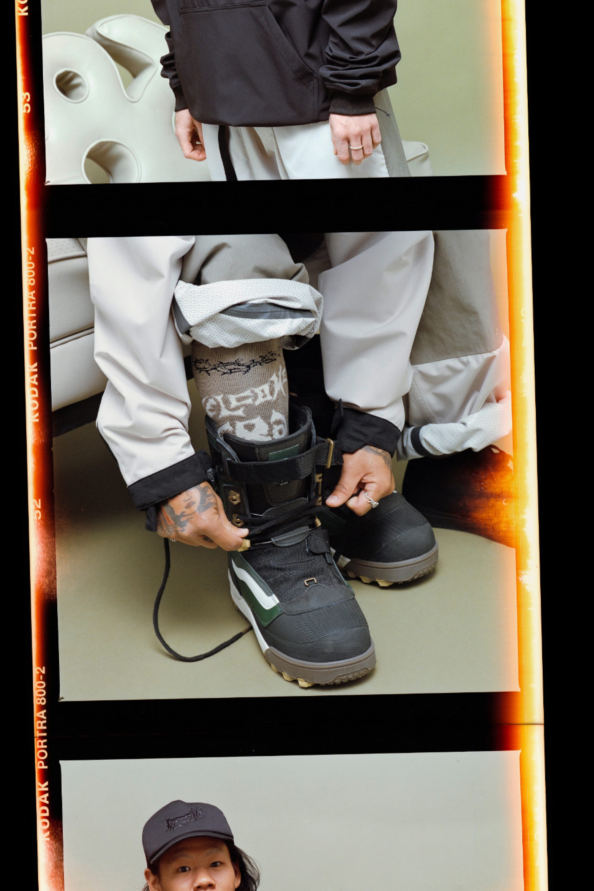 Someone in gray pants and a dark jacket laces up a black snow boot, revealing 686 x Welcome Socks - 2-Pack by 686. The image is split into three horizontal sections with an abstract light chair in the background.