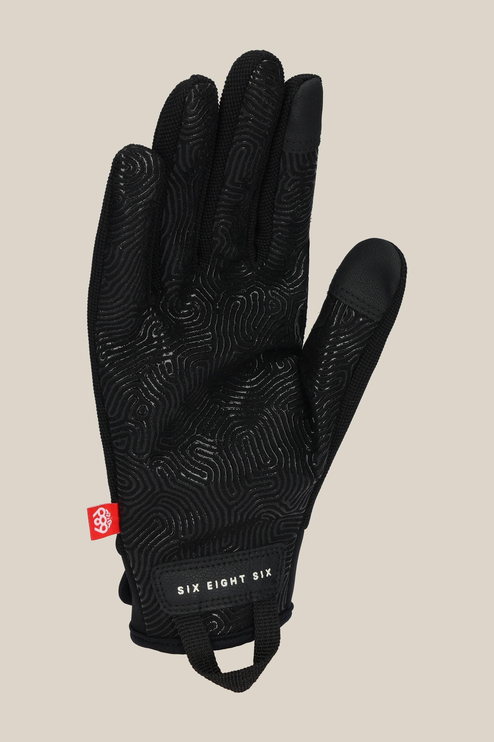The 686 Mens Outlaw Pipe Glove is black with a textured, wavy palm grip, a red side tag, and SIX EIGHT SIX in white on the wrist strap. Shown palm up against a beige background.