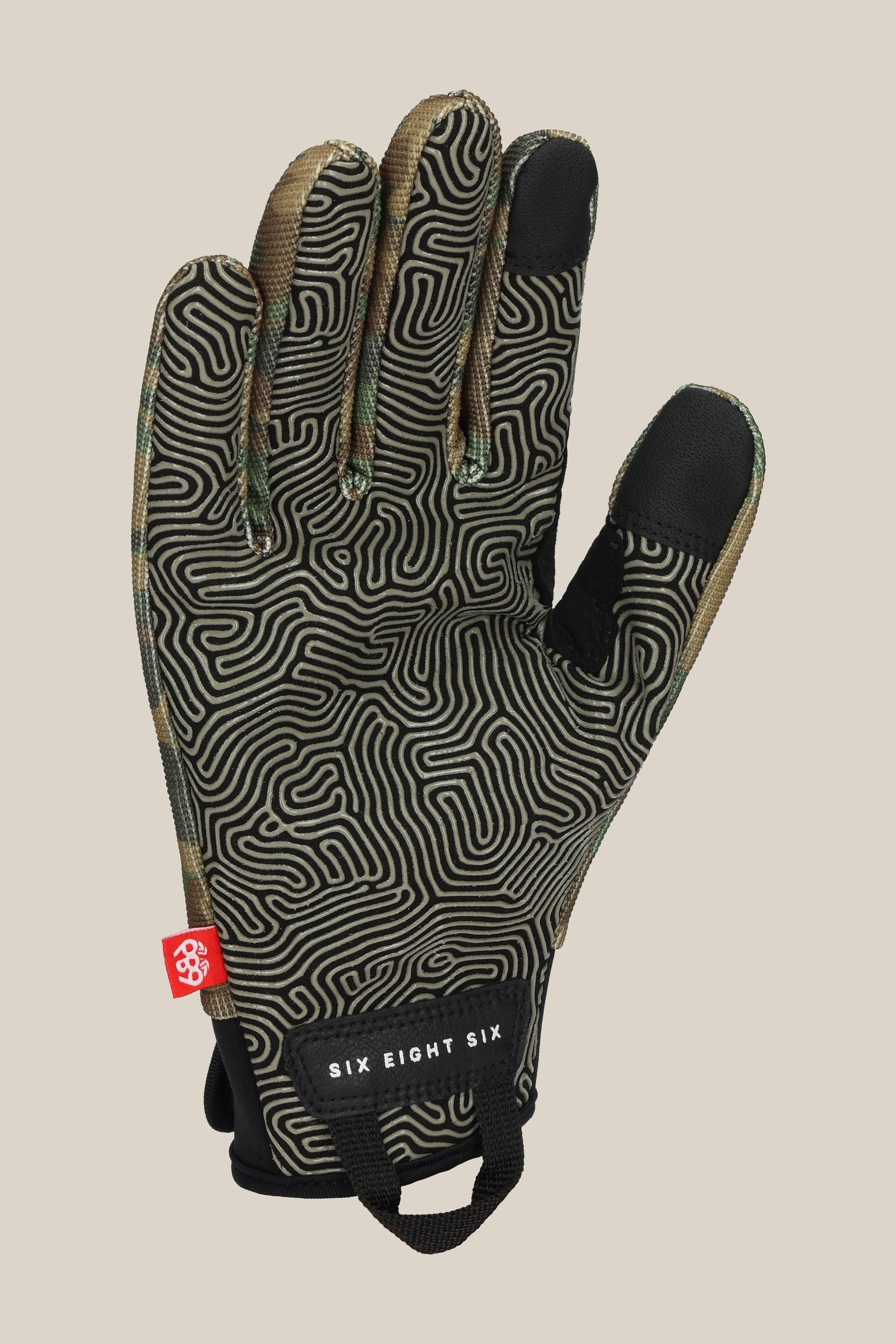 The 686 Mens Outlaw Pipe Glove in black features tan and green accents, a maze-like grip pattern, a small red side tag, and a SIX EIGHT SIX label near the wrist.