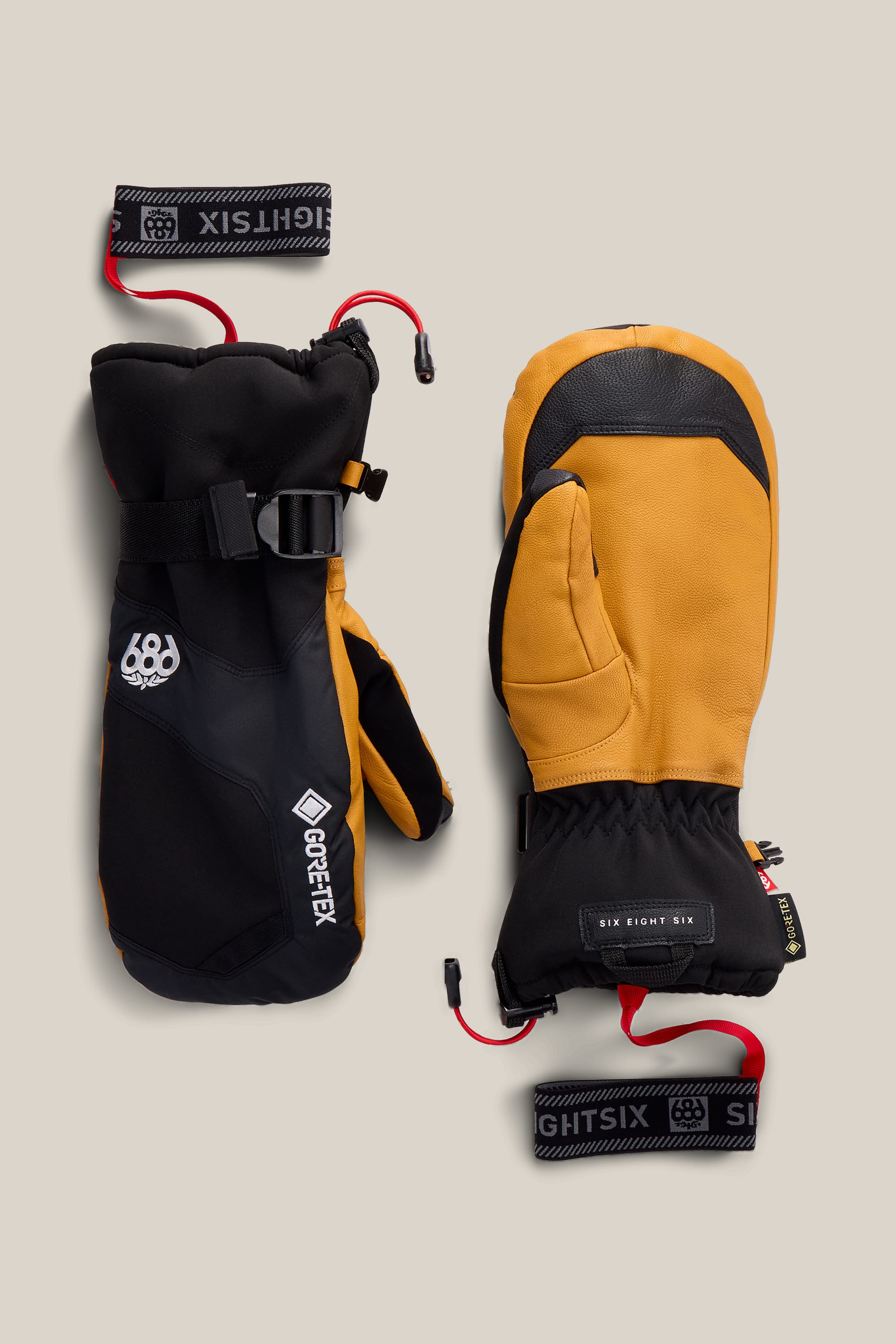 Two 686 Men’s GORE-TEX® Leather Linear™ Mitts, one in black and the other in tan with black accents, are displayed side by side on a beige background. Both mitts feature wrist straps labeled “686,” and the black mitten displays a GORE-TEX® logo.