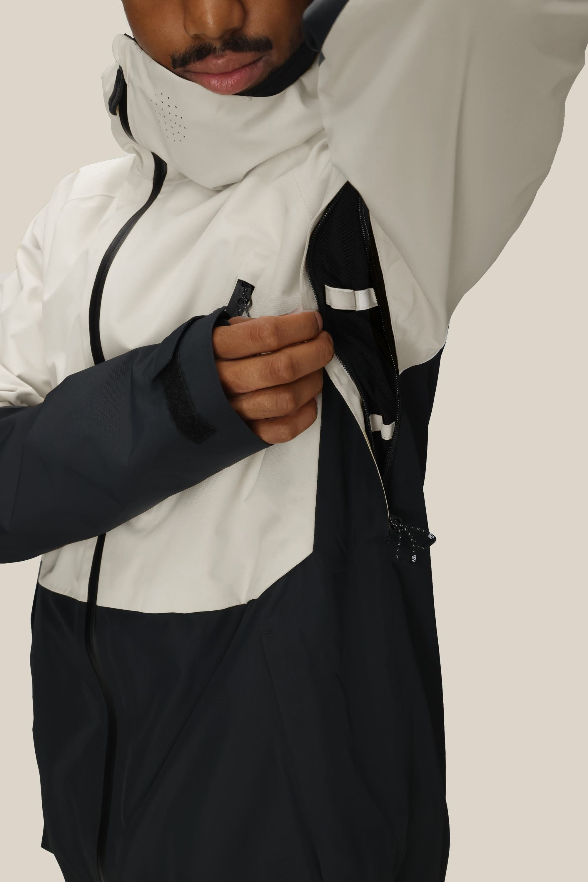 A person unzipping the underarm ventilation of the 686 Men’s Hydra™ Thermagraph® Jacket, highlighting its breathable feature. Only the lower part of their face and upper body are visible.