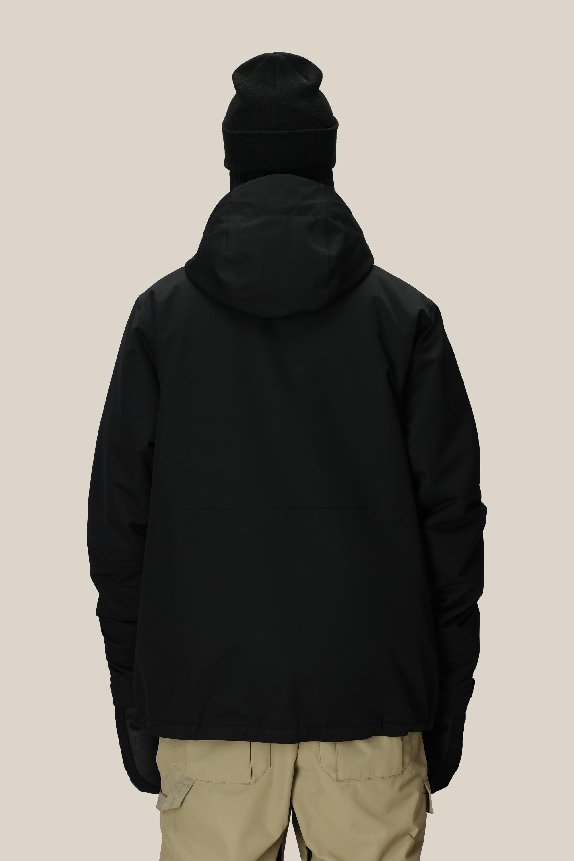 A person wearing the 686 Men’s Foundation™ Insulated Jacket in black, paired with a black beanie and light beige pants, is standing with their back to the camera against a plain, light background.