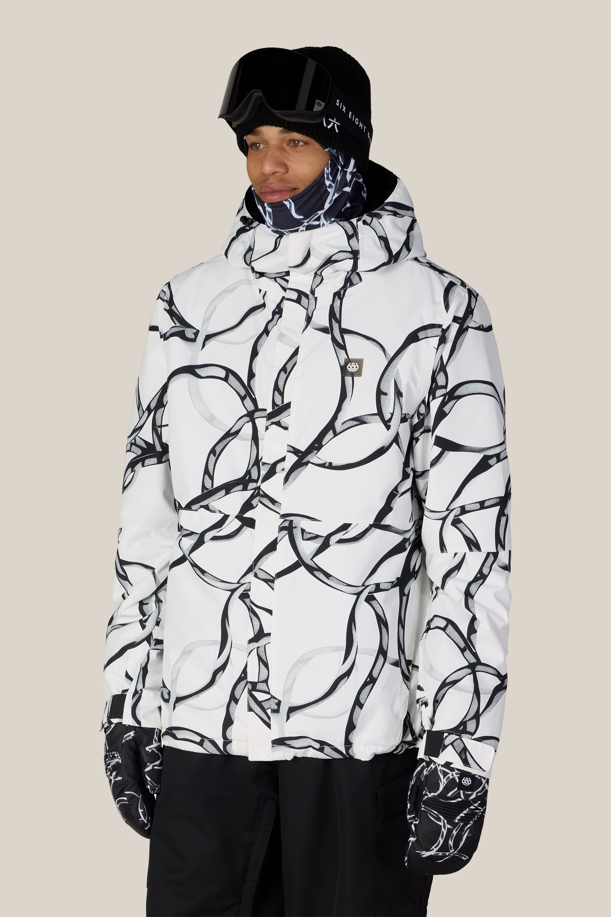 A person wearing the 686 Men’s Foundation™ Insulated Jacket by 686, paired with matching gloves, black ski goggles, and a black beanie, stands against a plain light background.