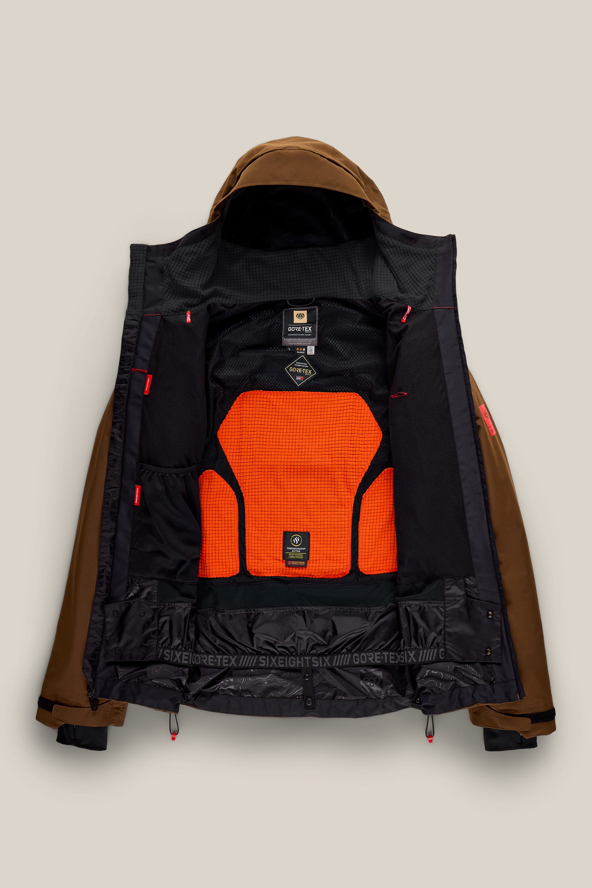 A 686 Men’s GORE-TEX® GT Thermagraph® Jacket in brown is laid flat, open to reveal its black and orange mesh interior lining with visible labels, pockets, and prominent 686 and GORE-TEX® branding.