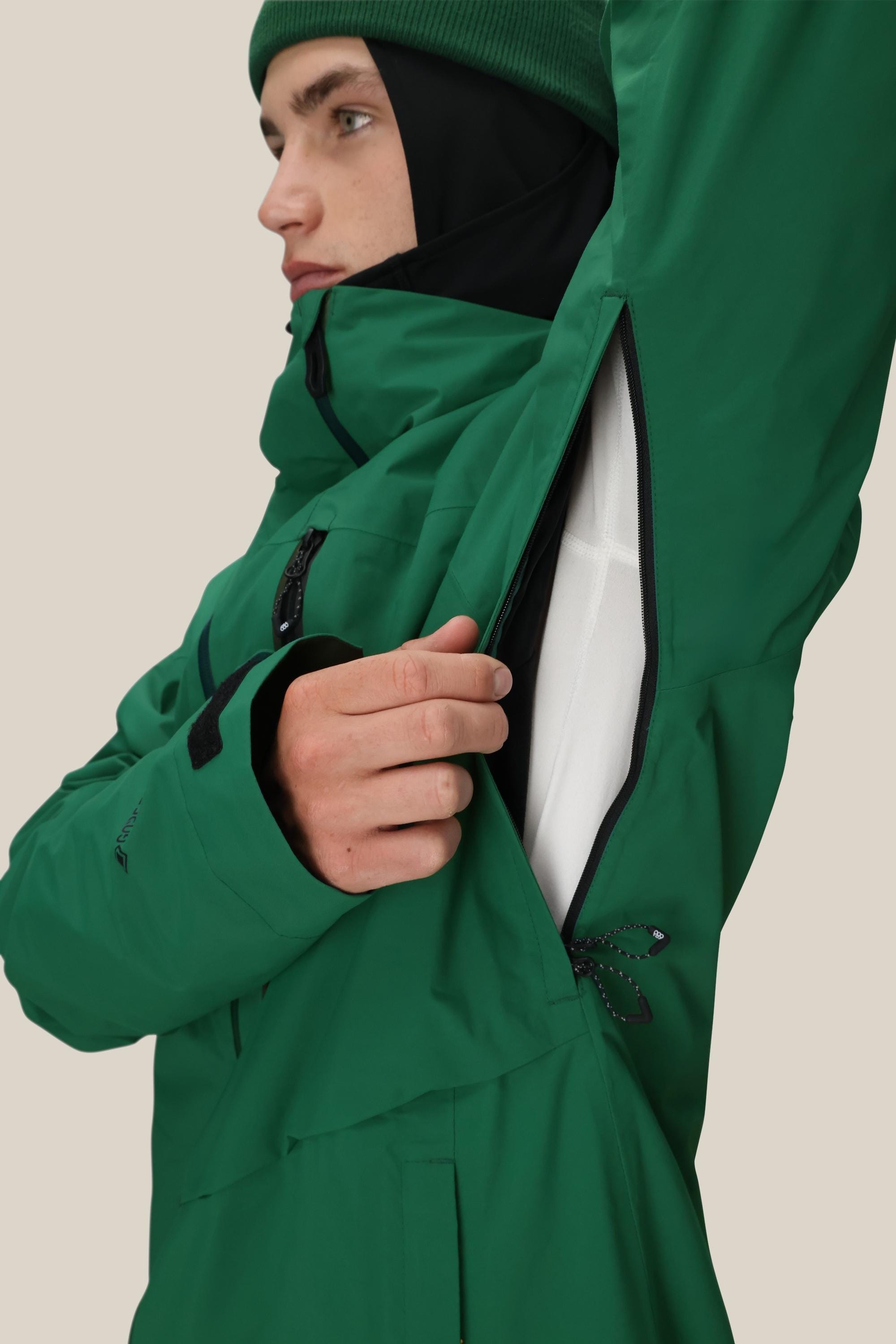 Wearing a 686 Mens GORE-TEX GT Thermagraph® Jacket and a beanie, a person opens the zippered underarm vent, revealing the jacket’s white inner lining.