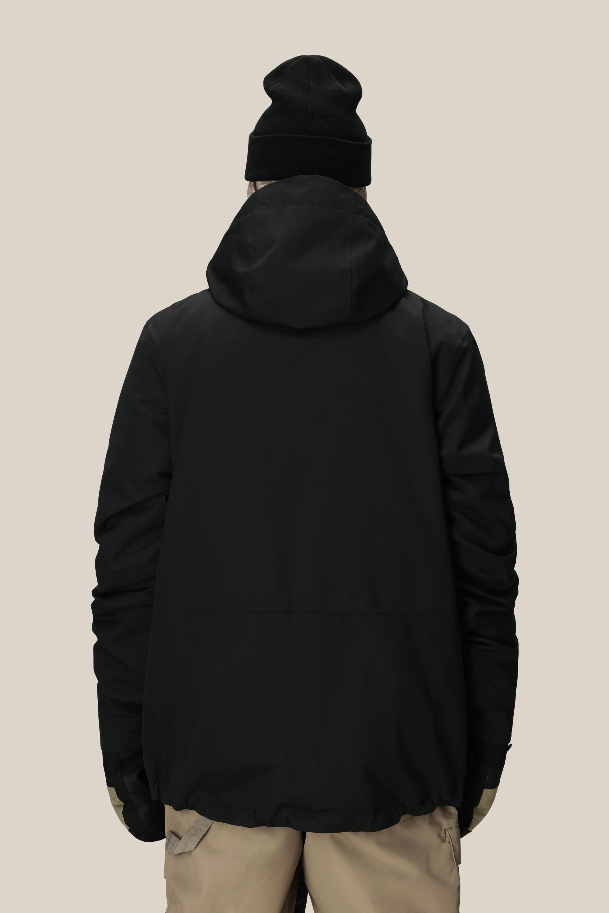 A person wearing the 686 Men’s SMARTY® 3-In-1 Form Jacket, along with beige pants, a black beanie, and gloves, is standing with their back facing the camera against a plain light background.