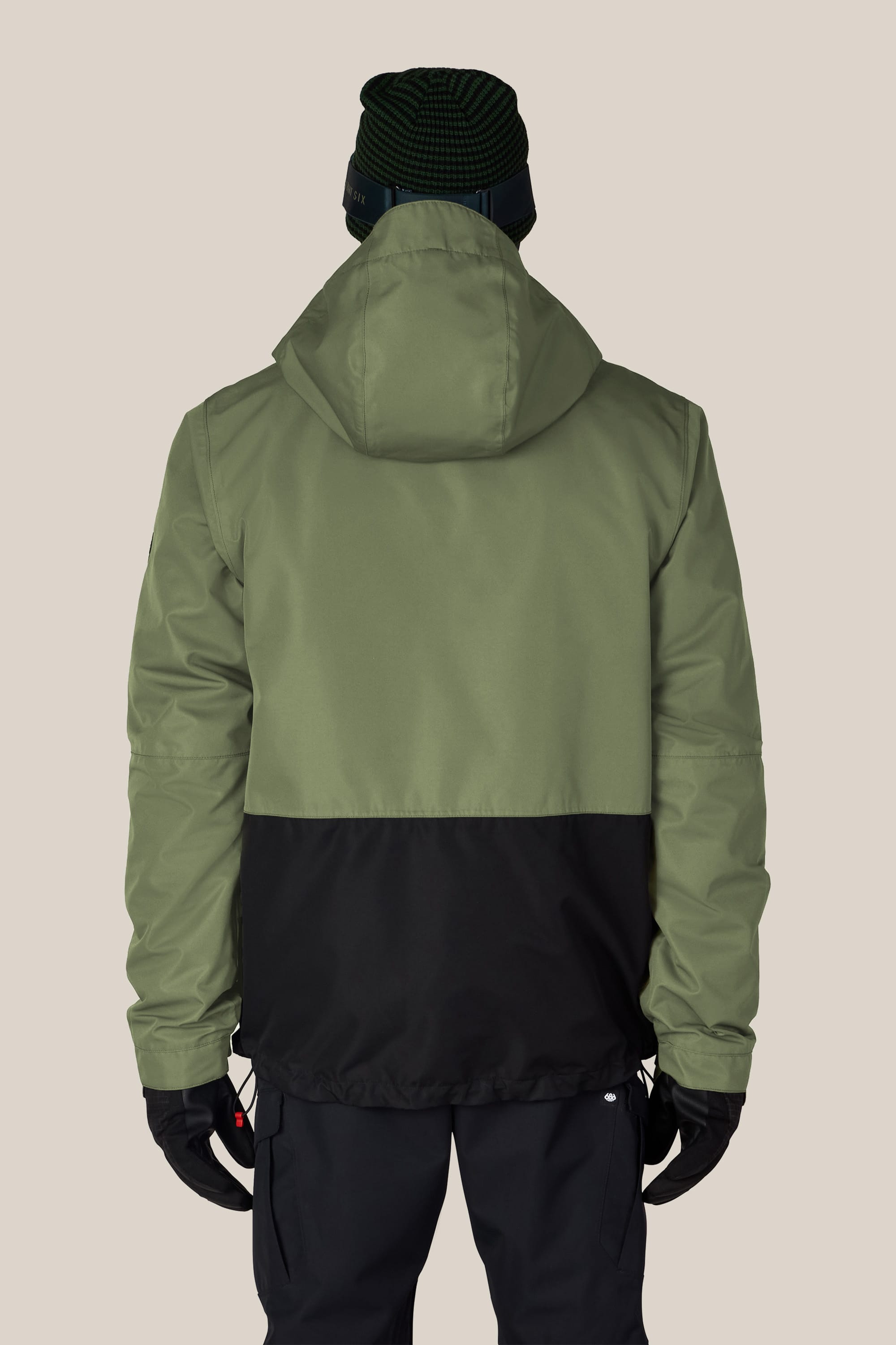 A person shown from the back against a plain light background is wearing the 686 Men’s SMARTY® 3-In-1 Form Jacket in green and black, paired with black pants, black gloves, and a dark green knit beanie.