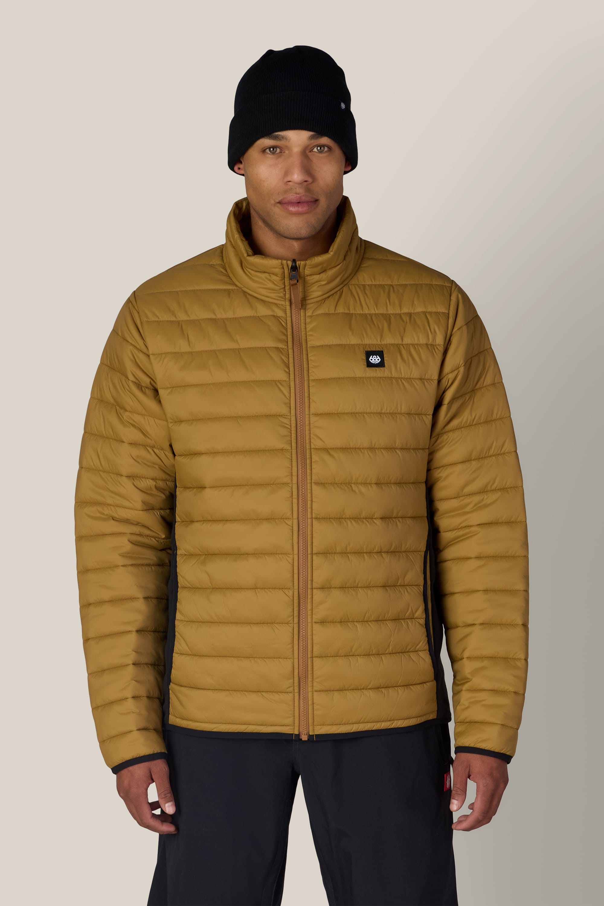 A man wearing a black beanie, black pants, and the 686 Men’s SMARTY® 3-In-1 Form Jacket by 686 stands against a light, neutral background.