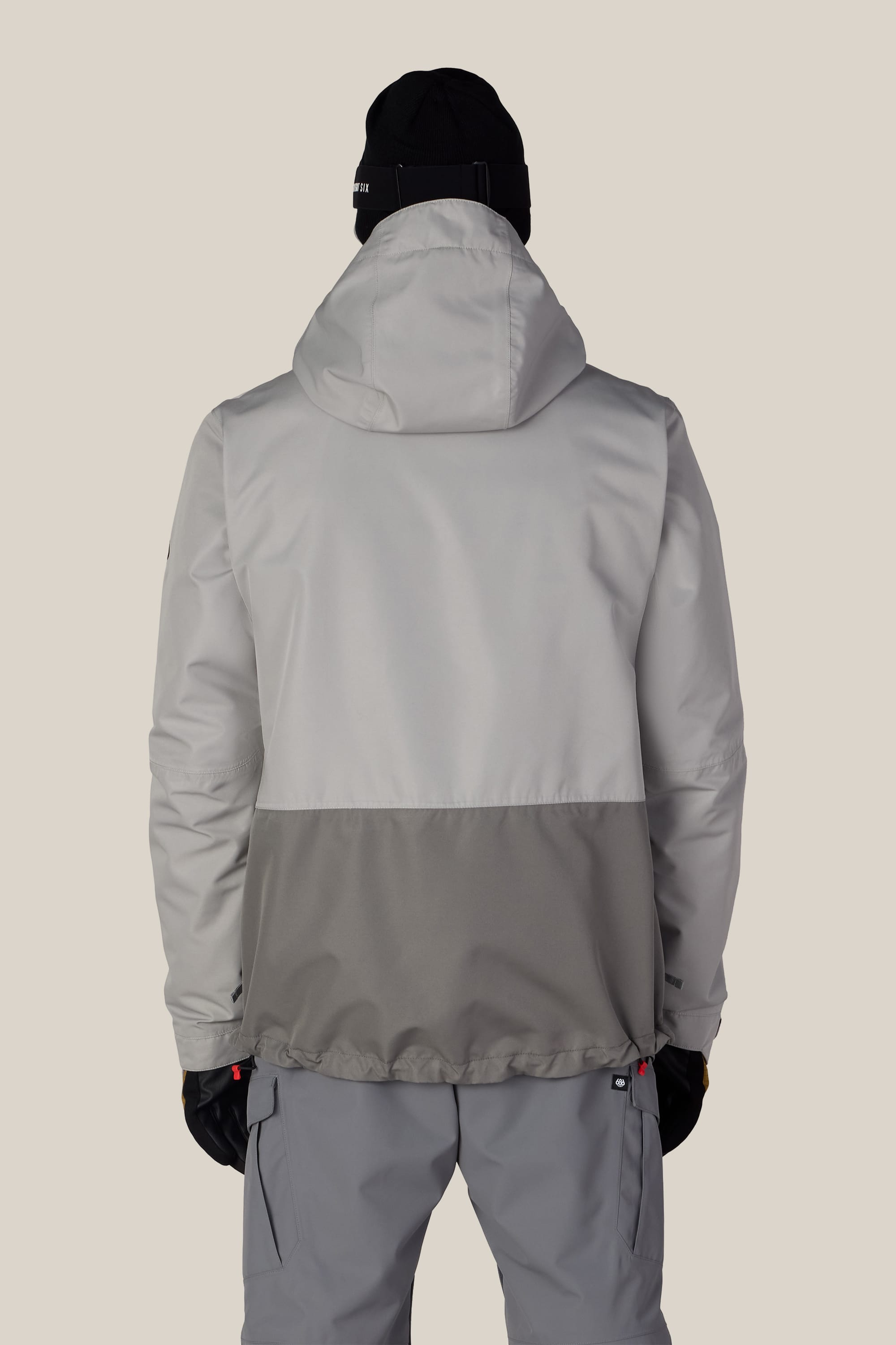 A person is shown from the back against a plain background, wearing the 686 Men’s SMARTY® 3-In-1 Form Jacket in gray and light gray, along with gray pants, black gloves, and a black beanie.