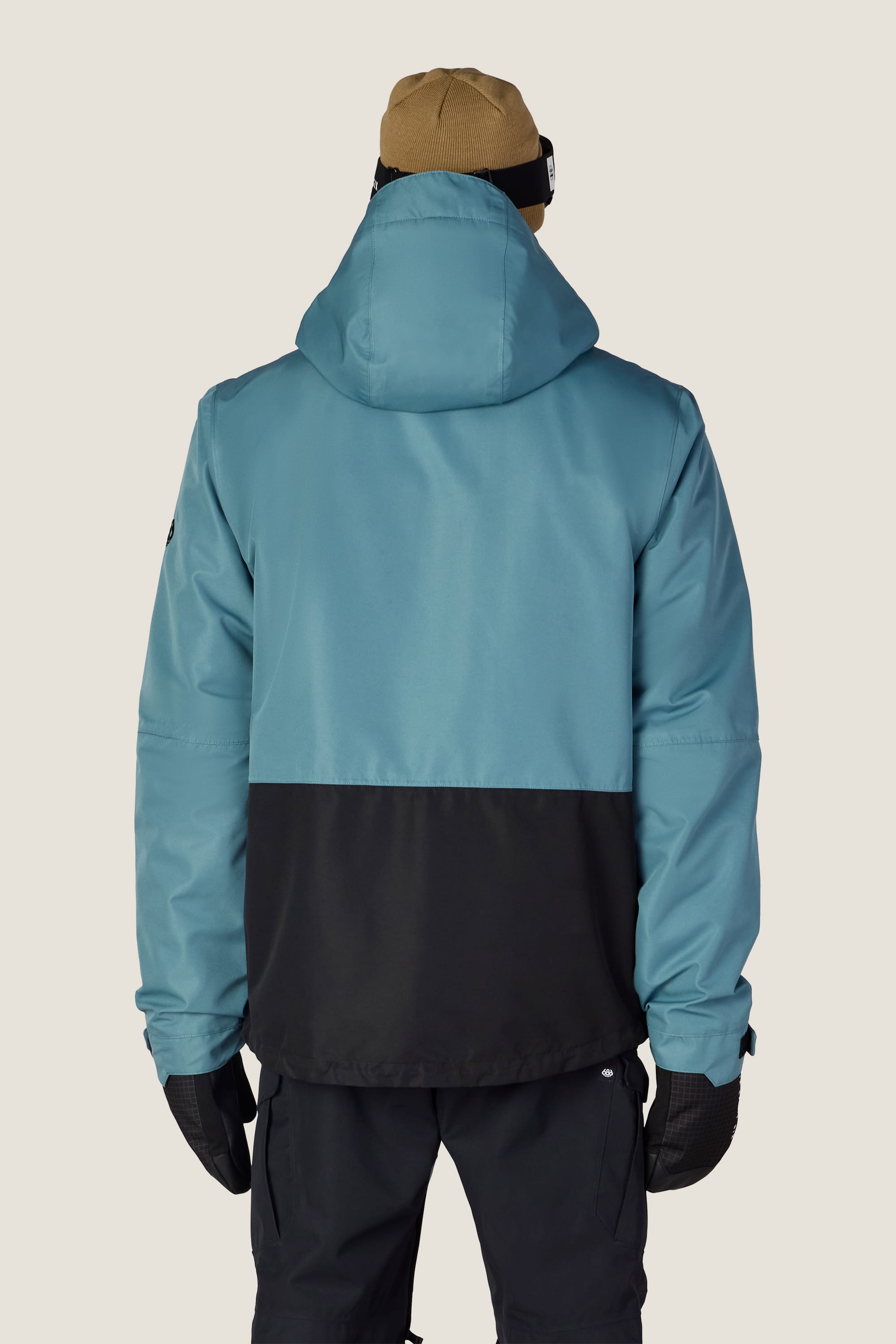 A person wearing the 686 Men’s SMARTY® 3-In-1 Form Jacket by 686, along with black pants, gloves, and a tan beanie, stands with their back to the camera against a plain background.
