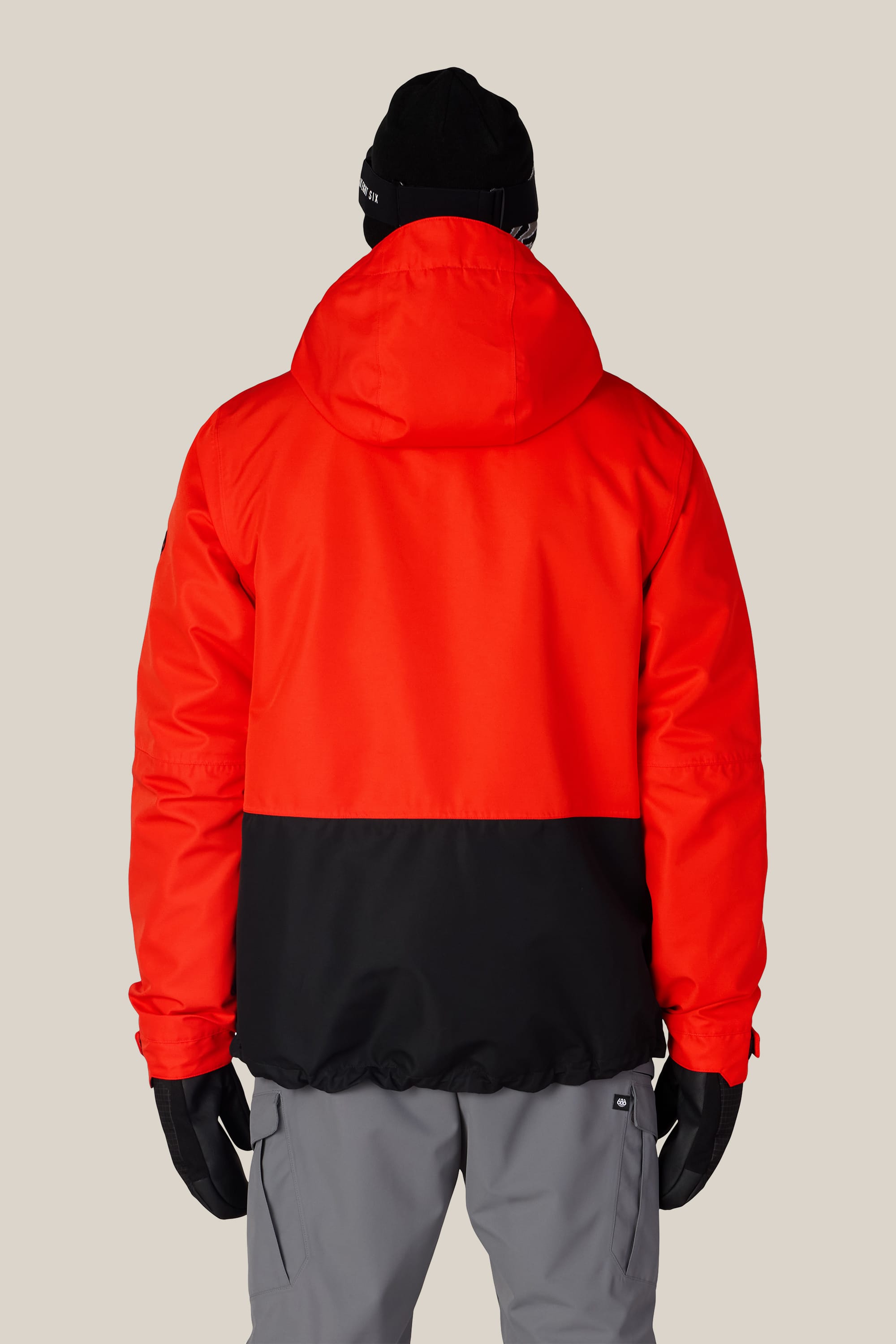 A person is shown from the back against a plain light background, wearing the 686 Men’s SMARTY® 3-In-1 Form Jacket in red and black, along with gray pants, black gloves, and a black beanie.