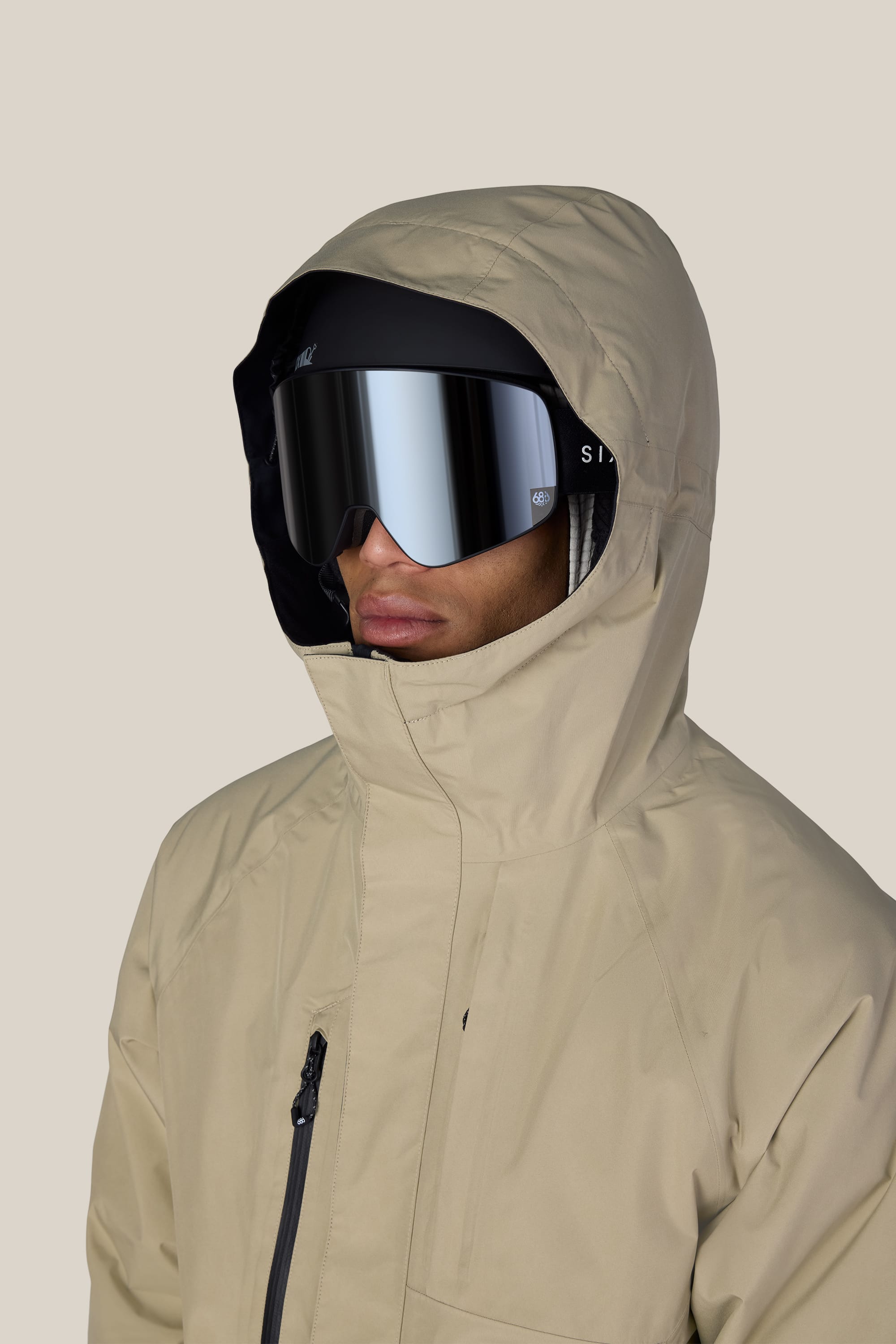 A person wearing the 686 Men’s GORE-TEX® Core Insulated Jacket in beige and reflective ski goggles, facing forward against a plain light background.