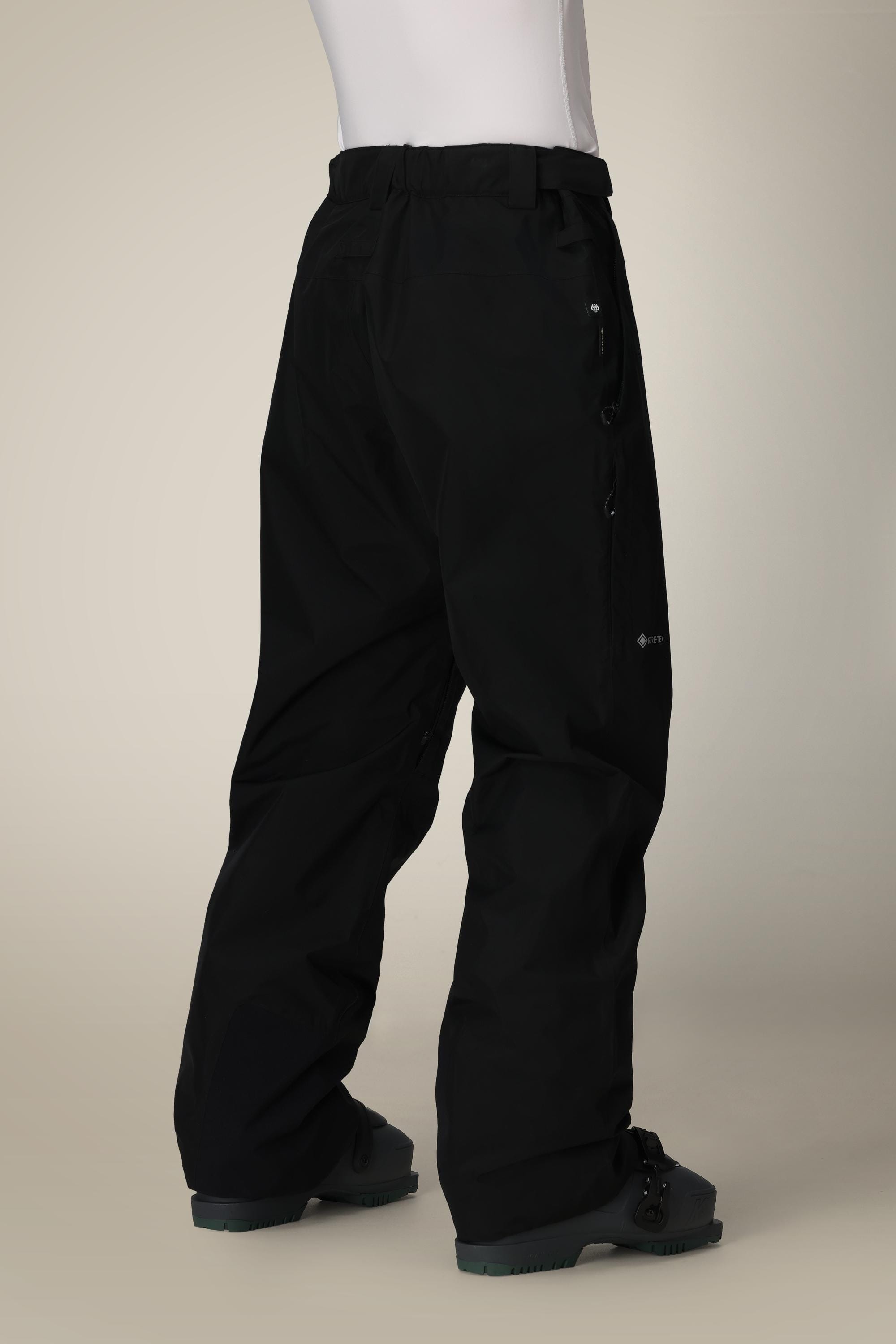 A person wearing 686 Mens GORE-TEX Core Shell Pant and black boots stands against a plain light background, facing away, with their upper body partially out of frame.