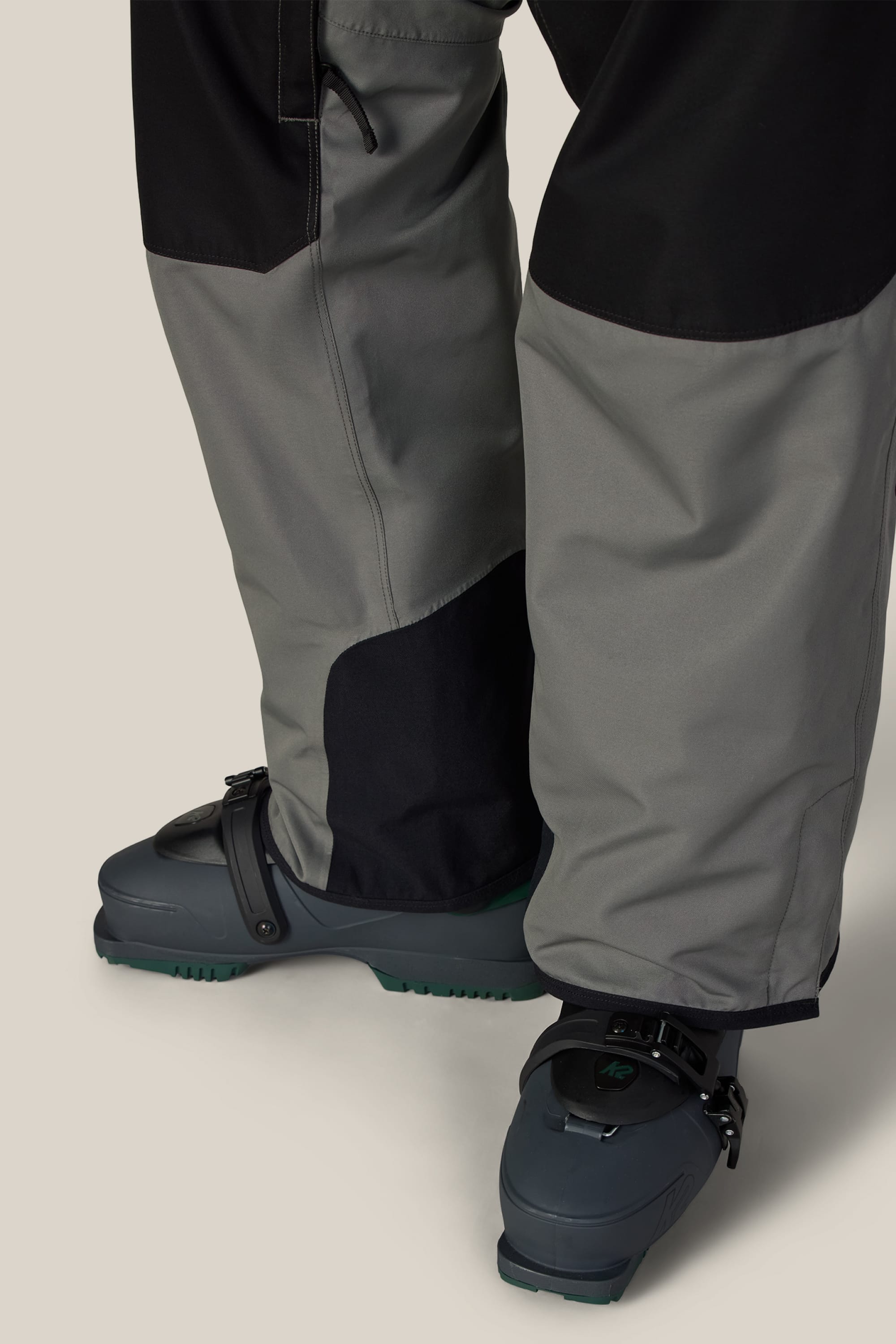Close-up of a person wearing 686 Men’s Hot Lap™ Insulated Bib ski pants in two-tone gray, shown from the knees down against a neutral background.
