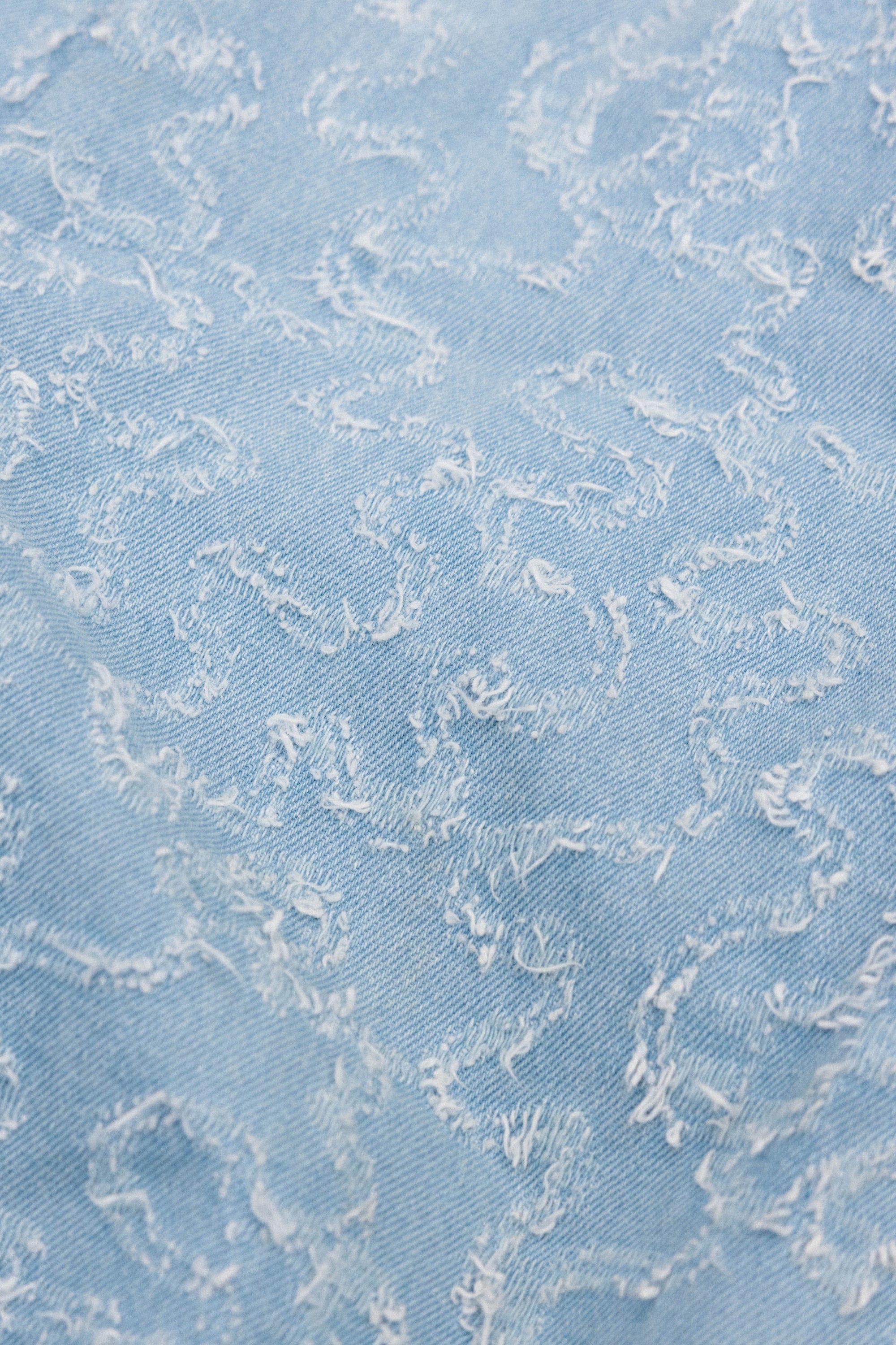 Close-up of the 686 Dojo® Frayed Denim Pant by 686, showcasing light blue denim with a textured, frayed pattern and irregular, wavy lines for a distinct distressed look—perfectly styled with men’s woven pants.