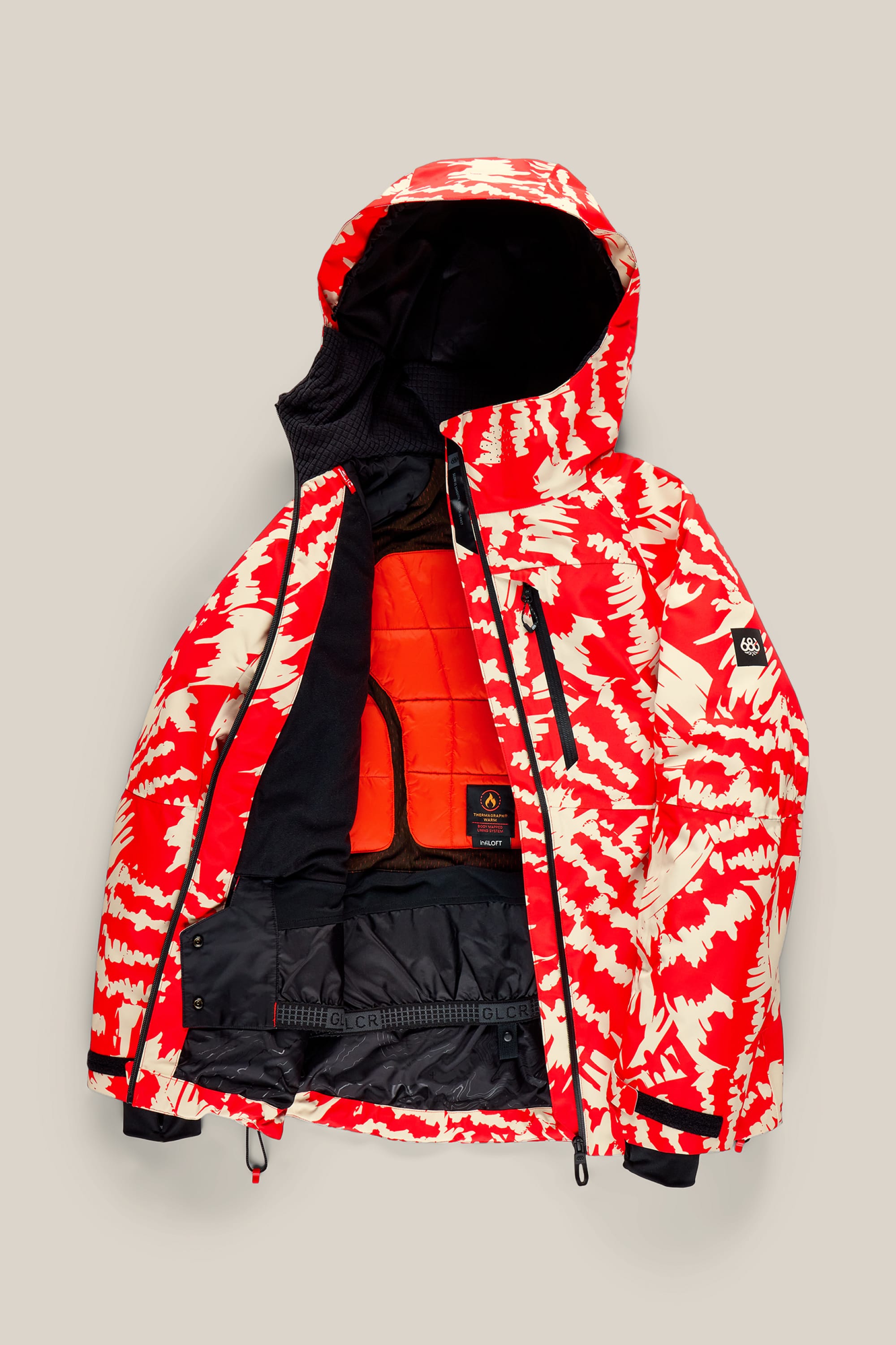 The 686 Women’s Hydra™ Thermagraph® Jacket by 686 is shown open against a neutral background, featuring a red and cream pattern, hood, black interior lining, zippered pockets, and an inner orange insulated layer.