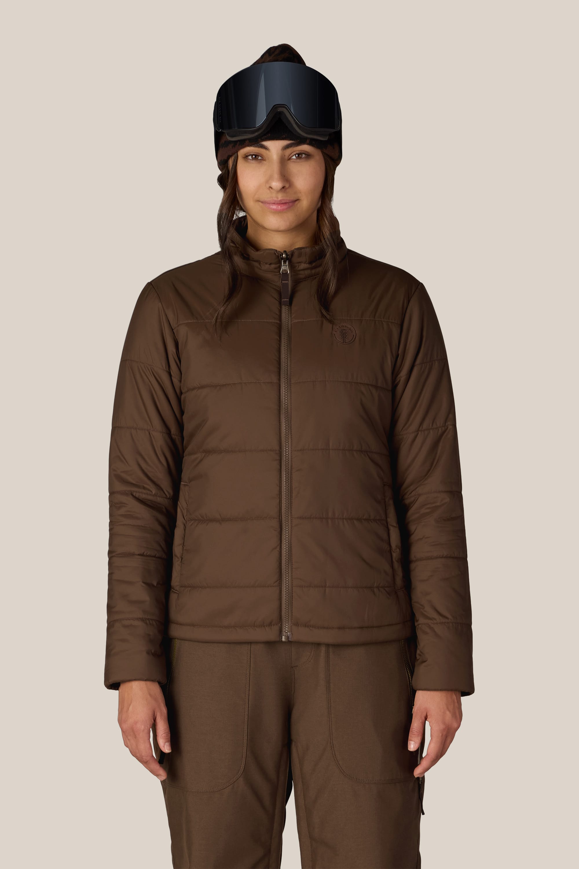 A person stands facing forward against a plain light background, wearing the 686 Women’s SMARTY® 3-In-1 Spellbound Jacket and matching pants from 686, paired with black ski goggles.