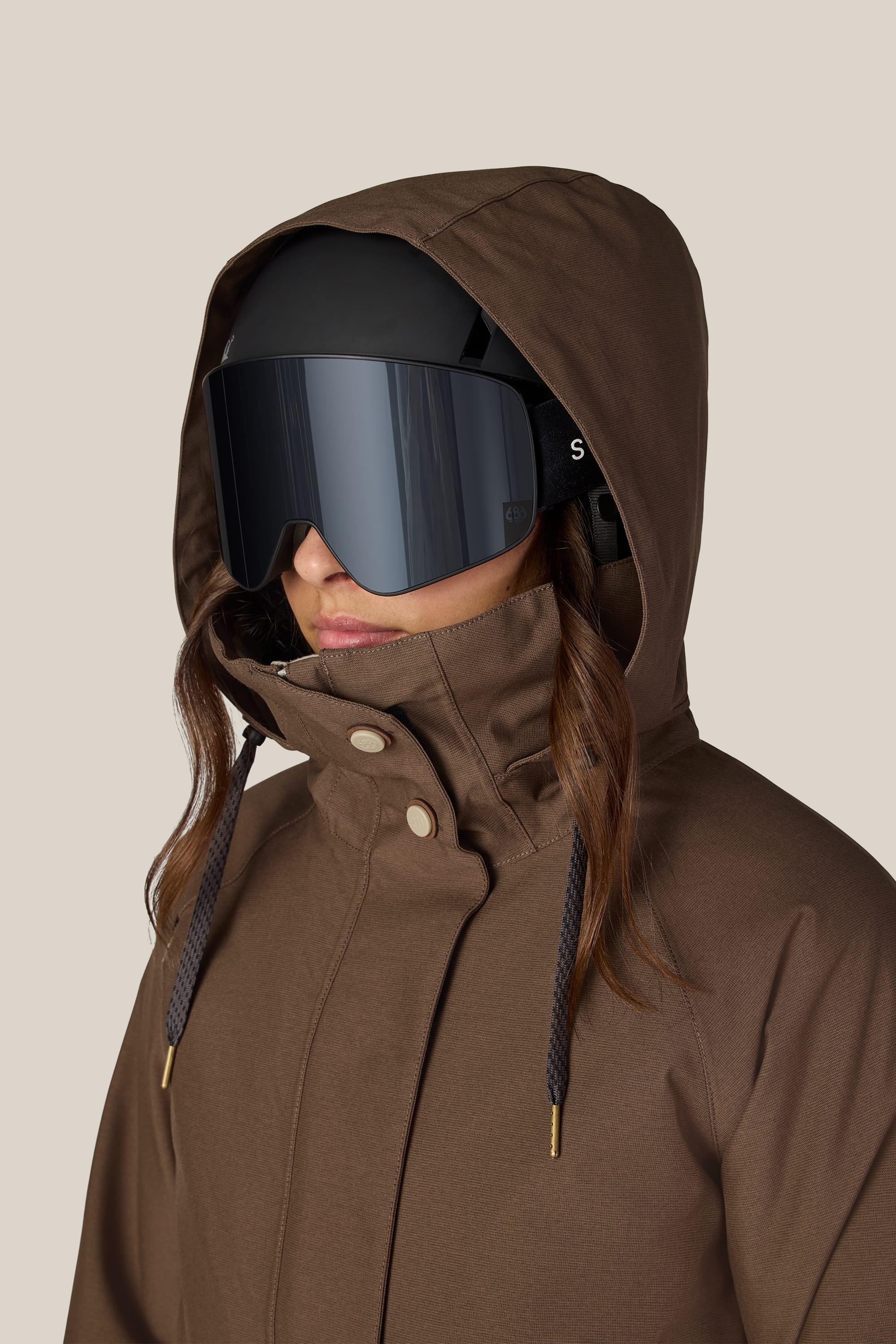 A woman wearing the 686 Women’s SMARTY® 3-In-1 Spellbound Jacket by 686, paired with a black ski helmet and large reflective ski goggles, faces left against a plain, light-colored background.