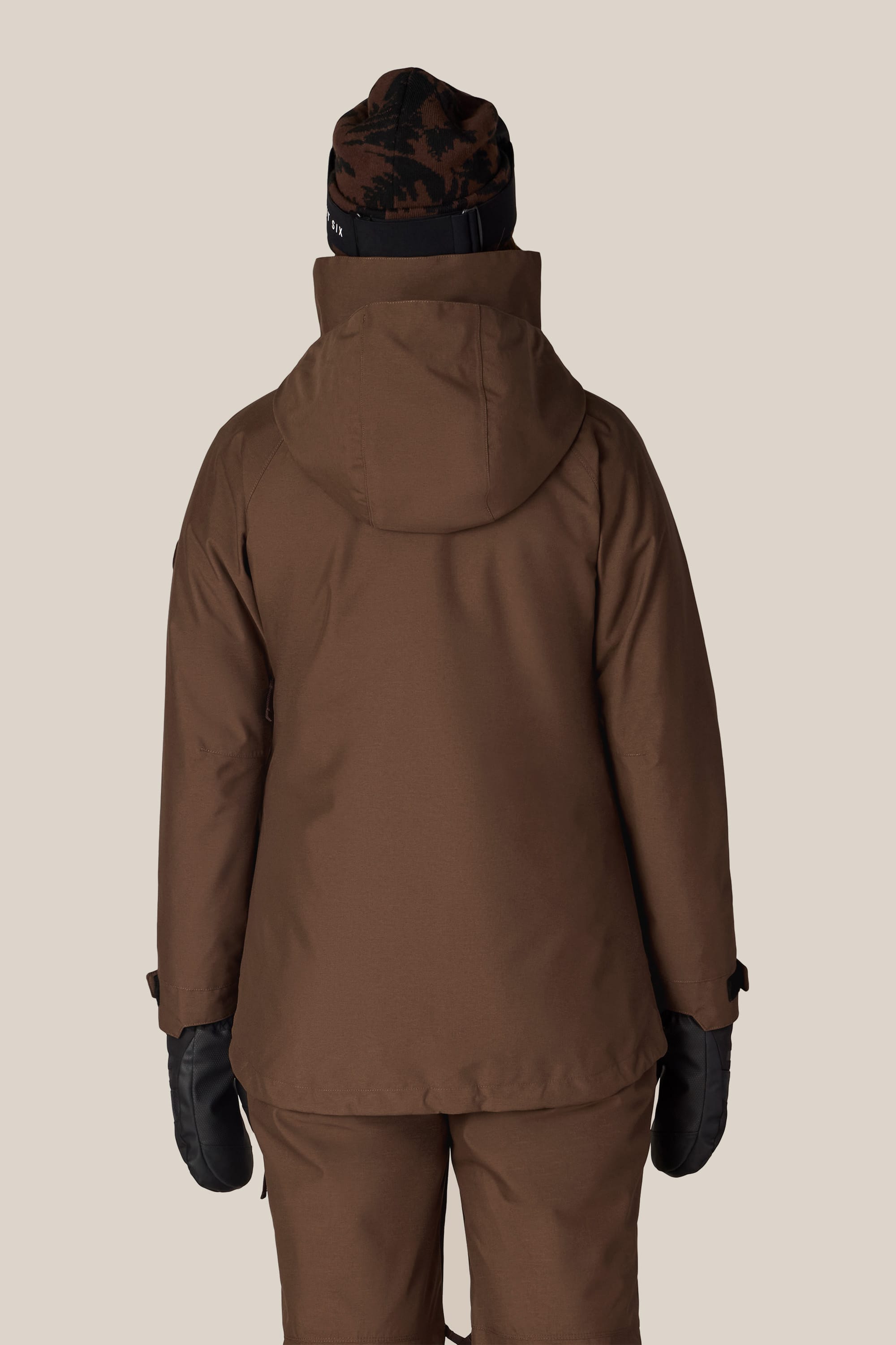A person is seen from behind against a plain light background, wearing the 686 Women’s SMARTY® 3-In-1 Spellbound Jacket by 686, paired with matching pants, black mittens, and a black and brown beanie.