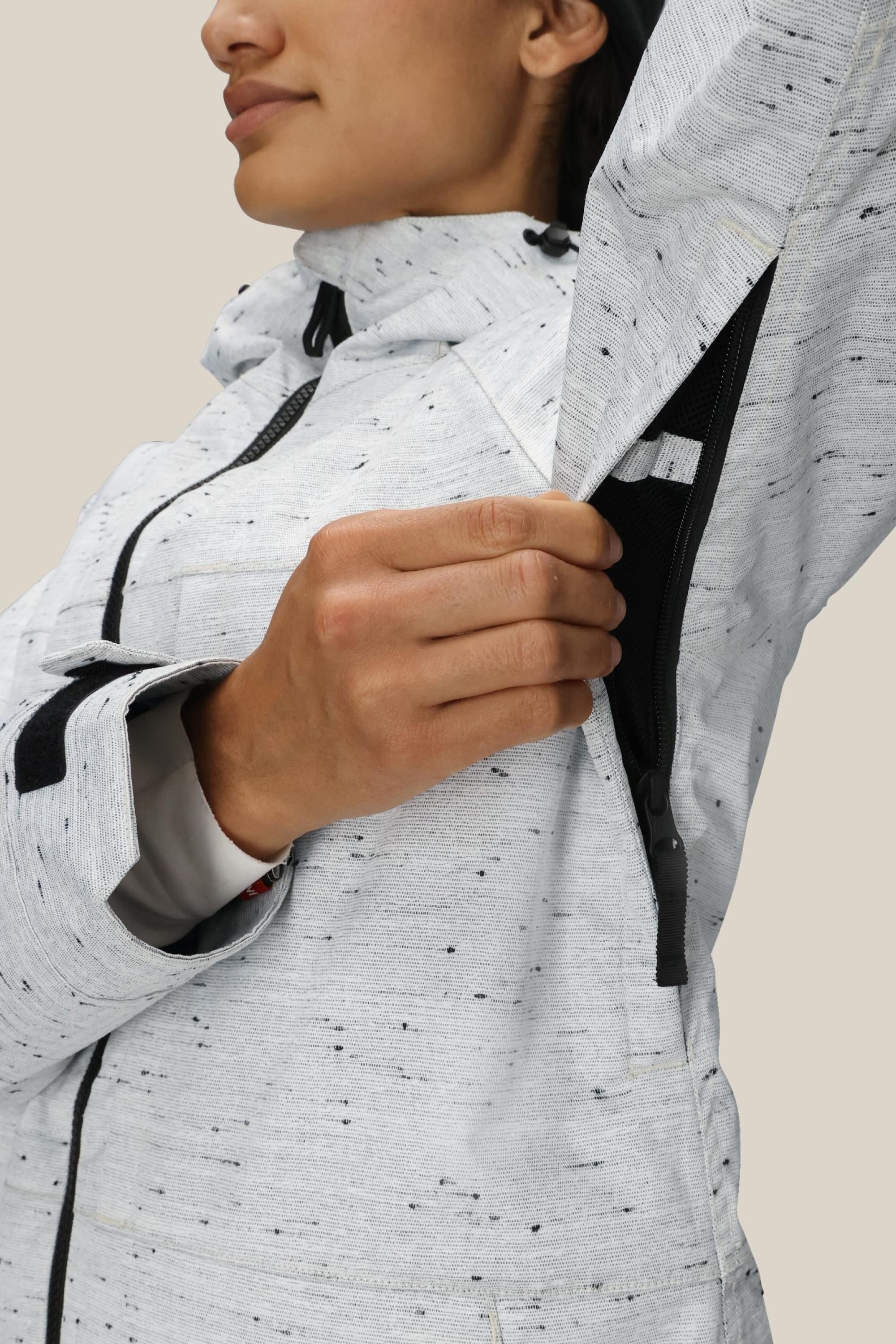 A person opens the underarm zipper vent of the 686 Women’s Athena™ Insulated Jacket in light gray speckle, revealing the mesh lining inside. The focus is on their hand pulling the zipper and the detailed texture of the 686 jacket’s material.