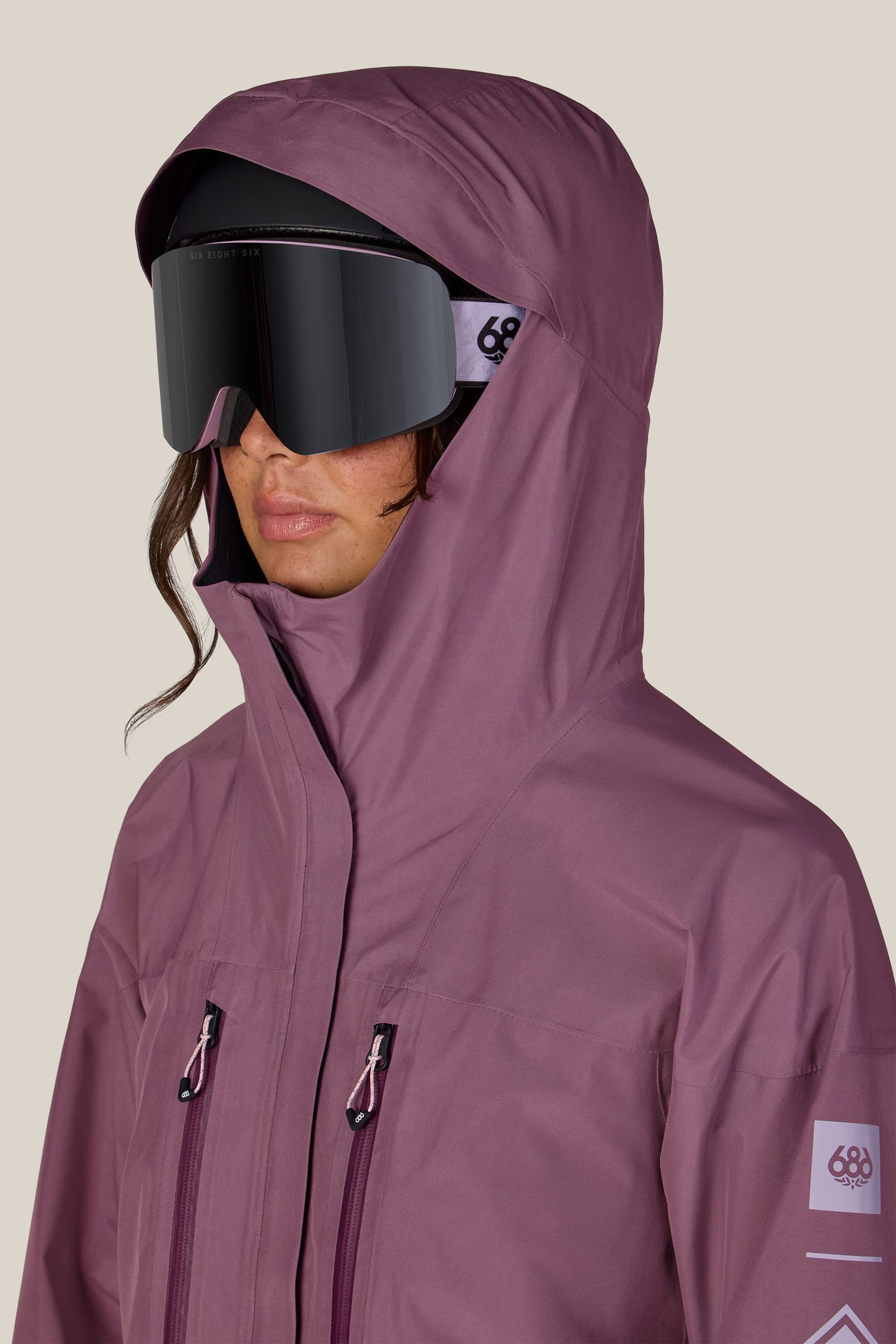 A person is wearing the 686 Women’s GORE-TEX® Skyline Thermagraph® Jacket by 686 along with large black ski goggles, standing against a plain background.