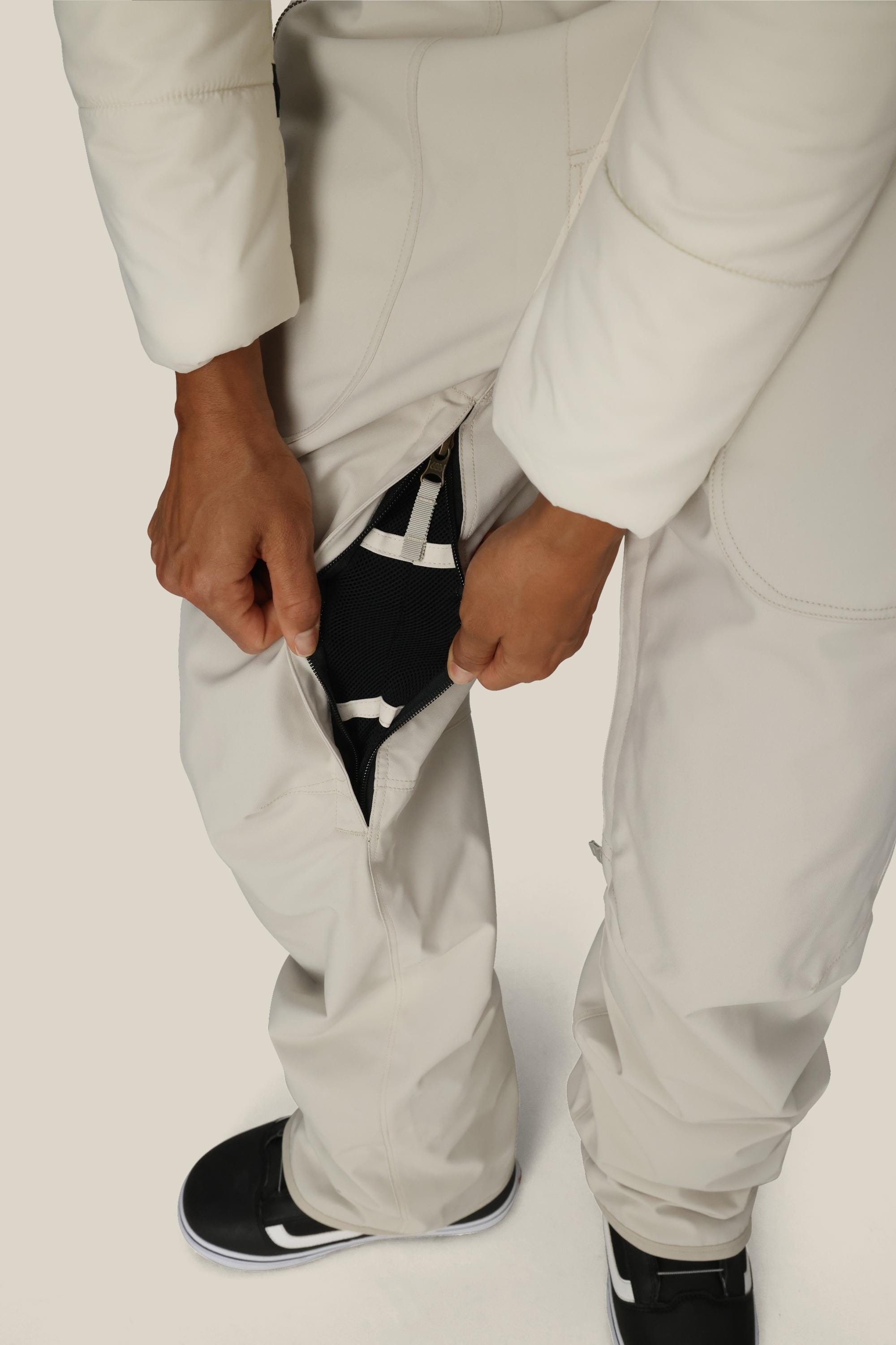 A person wearing the 686 Women’s Black Magic™ Insulated Bib demonstrates the leg zipper opening to reveal a black mesh layer underneath. The individual’s hands are holding the zipper, and only the lower body is shown.