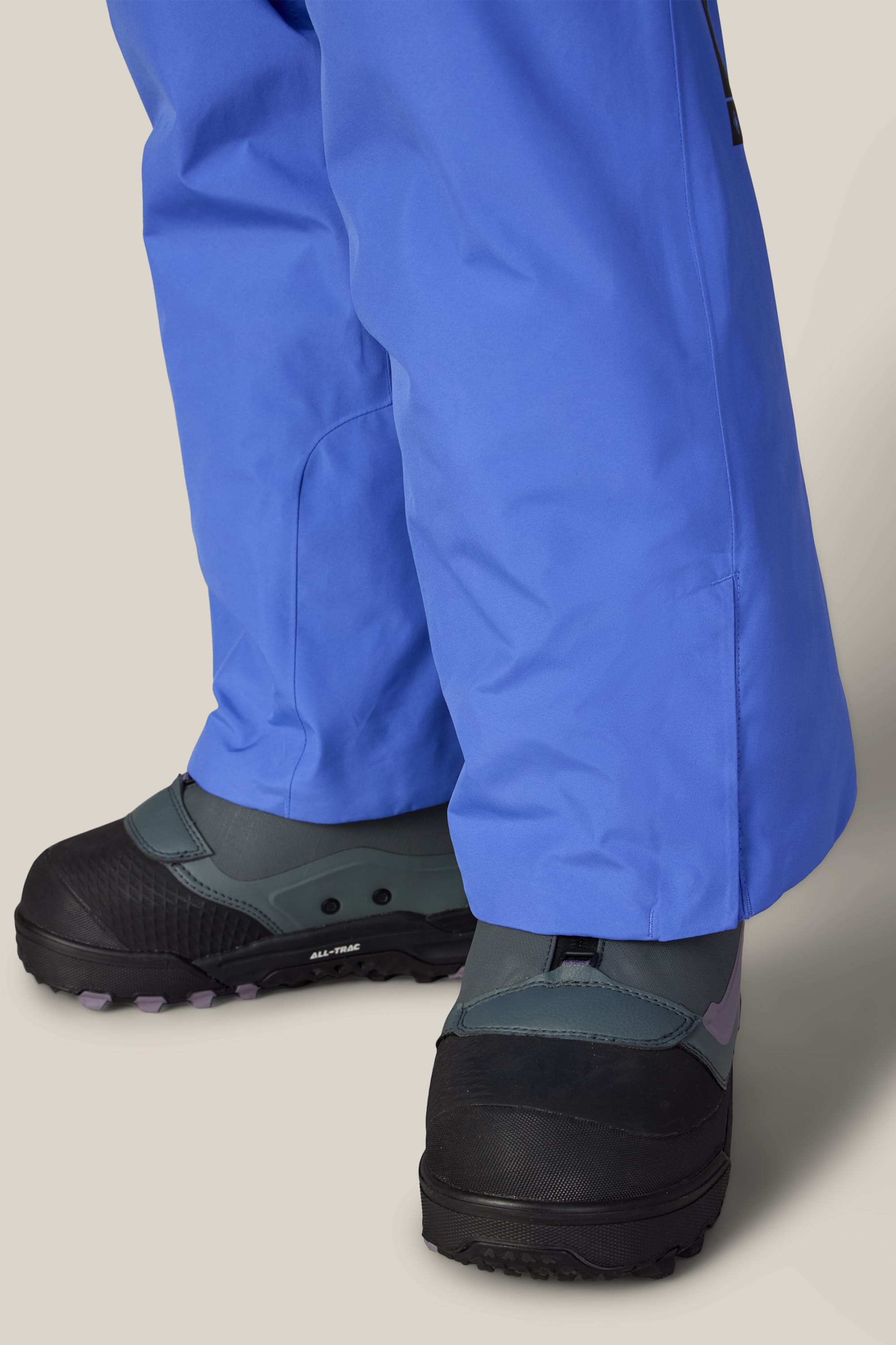 A person wearing the 686 Women’s GORE-TEX® Willow™ Insulated Pant in blue and black winter boots with gray and purple details, standing on a light background.