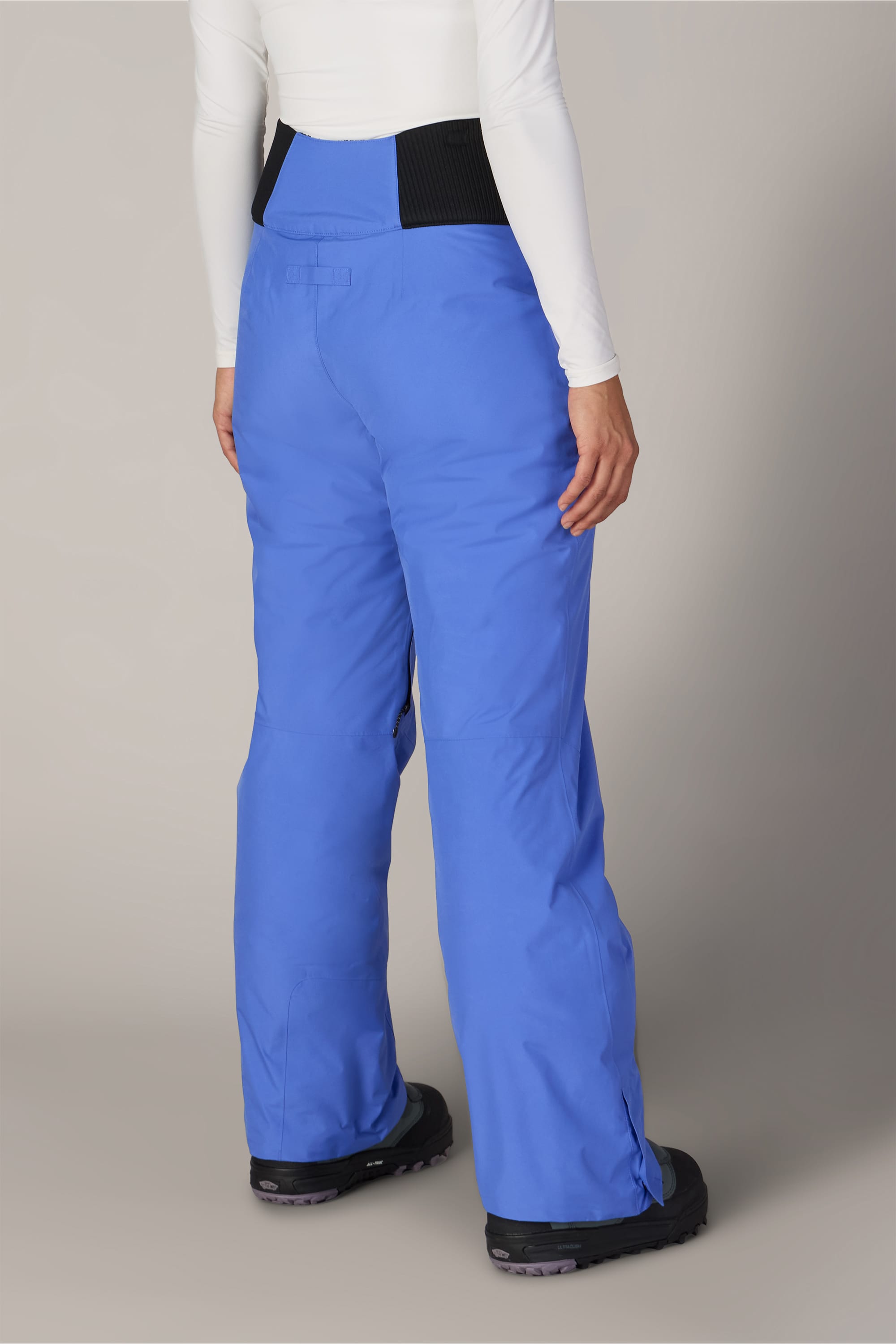 A person is shown from the back against a plain background, wearing the 686 Women’s GORE-TEX® Willow™ Insulated Pant in bright blue, paired with black boots and a white long-sleeve shirt.
