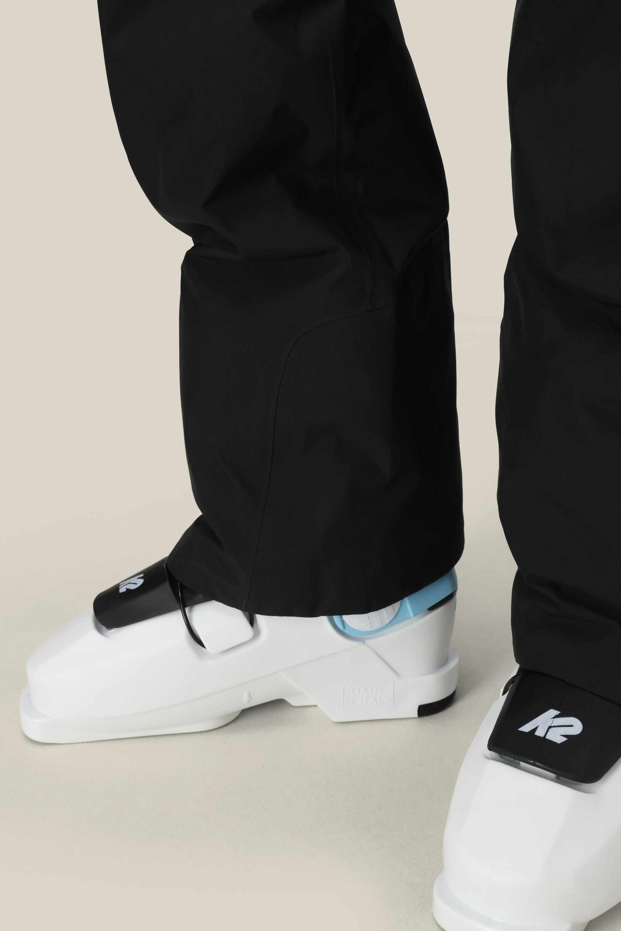 A person wearing 686 Women’s GORE-TEX® Willow™ Insulated Pant in black and white K2 ski boots, viewed from the side on a light background.