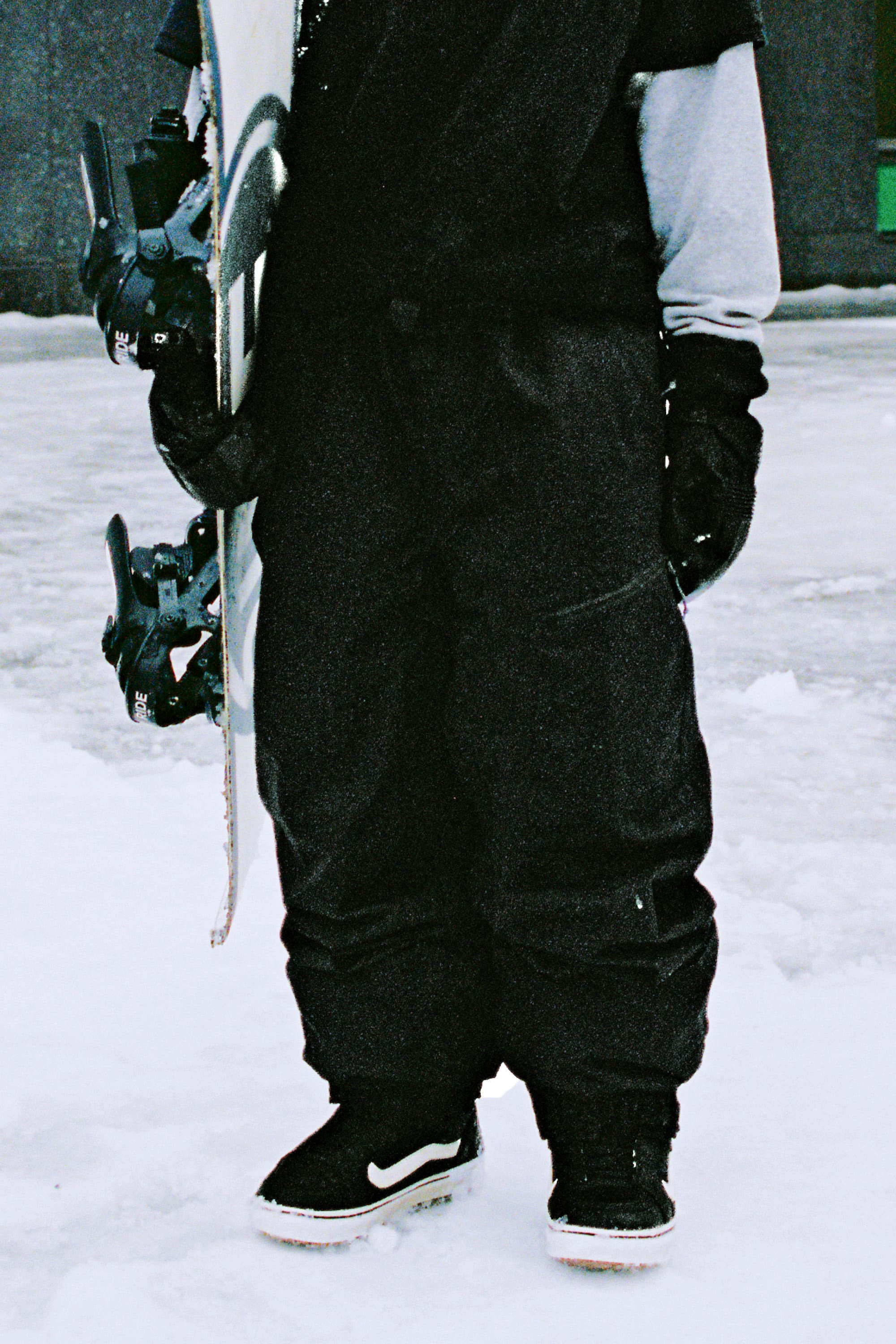 Wearing 686 Women's Outline™ Shell Pant, a person stands on snow holding a snowboard upright. Black gloves and black-and-white boots are also visible, but the person’s upper body and face are not shown.