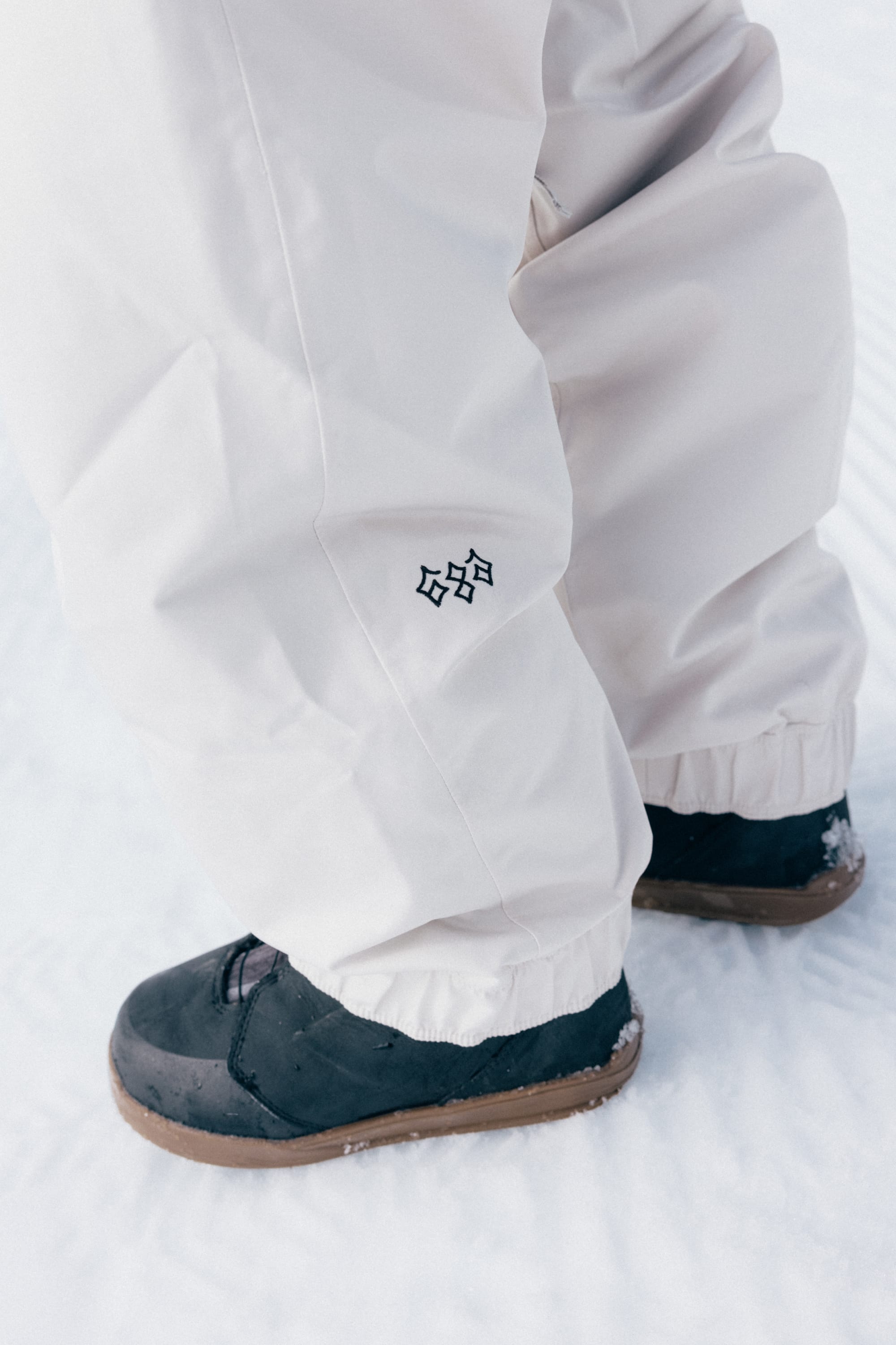 A person is wearing 686 Women’s Outline™ Shell Pant by 686 and black winter boots while standing on snow.