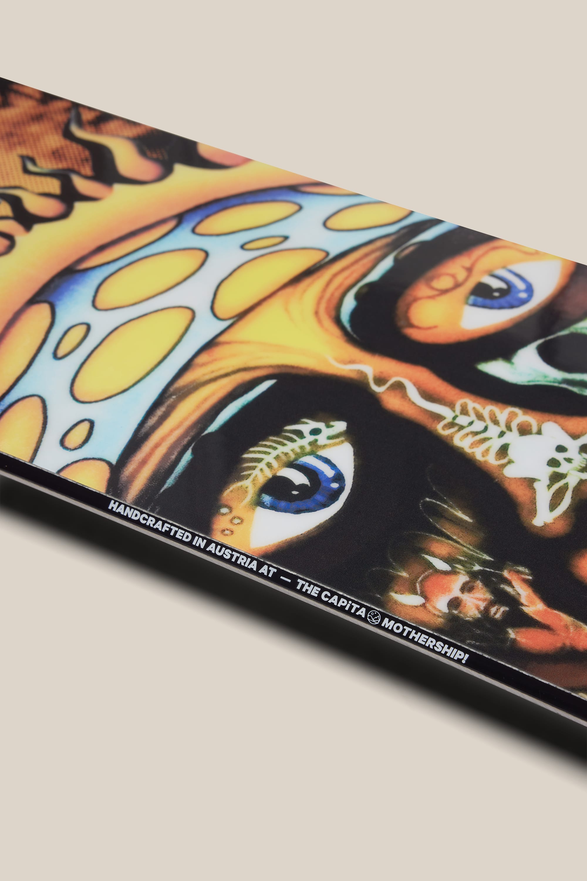 Close-up of the 686 Sublime Snowboard by 686, showcasing vibrant, surreal artwork with two detailed eyes and abstract colorful patterns. Text along the edge reads: HANDCRAFTED IN AUSTRIA AT - THE CAPITA MOTHERSHIP!.