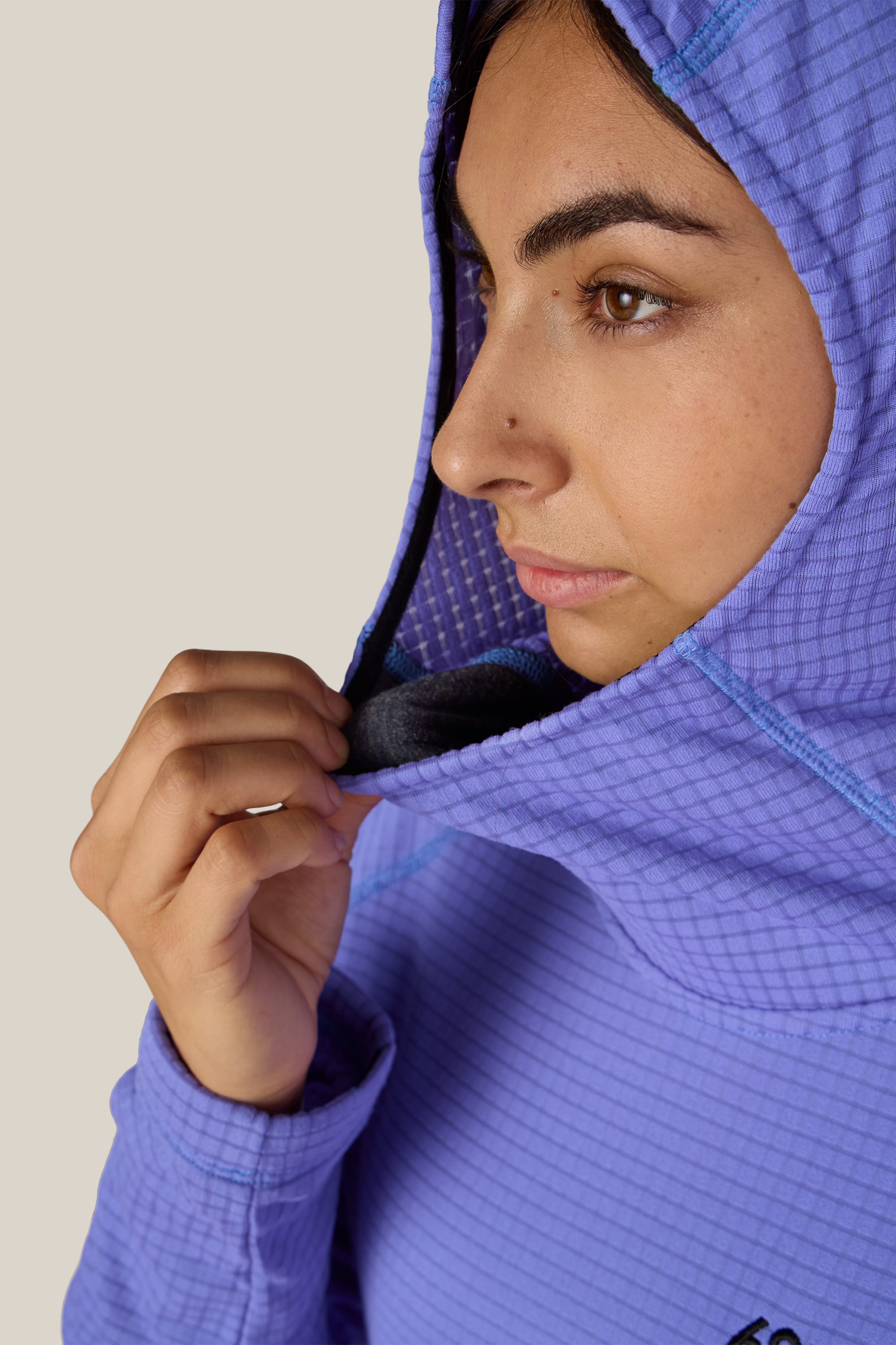A person wearing the 686 Women’s Mission Grid™ Hoody, a purple textured polyester knit jacket from 686, holds the edge of the hood, partially covering their head against a plain, light-colored background.