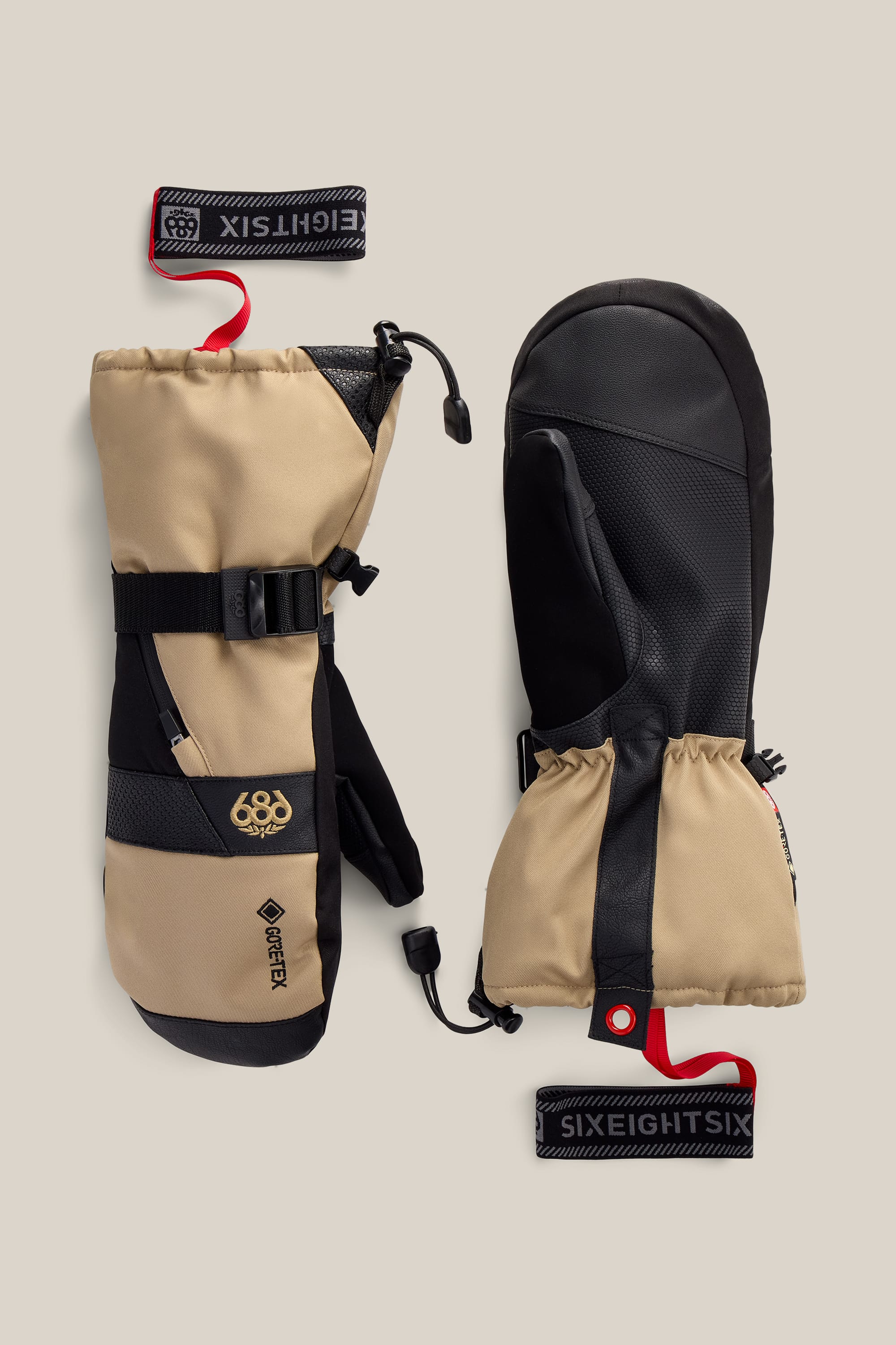 A pair of beige and black 686 Men’s GORE-TEX® SMARTY® 3-In-1 Gauntlet Mitts with adjustable straps and red 686 wrist leashes displayed on a neutral background.