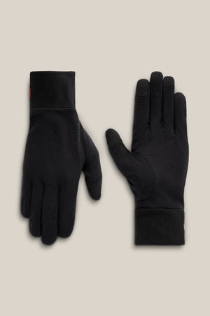 A pair of 686 Men’s Merino Glove Liners in black is shown on a light beige background; one glove displays the palm side, while the other reveals the back.