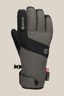 The 686 Mens GORE-TEX Linear Under Cuff Glove, shown in gray and black with small logos, a GORE-TEX tag, and an adjustable wrist strap, offers excellent winter protection and is photographed against a beige background.