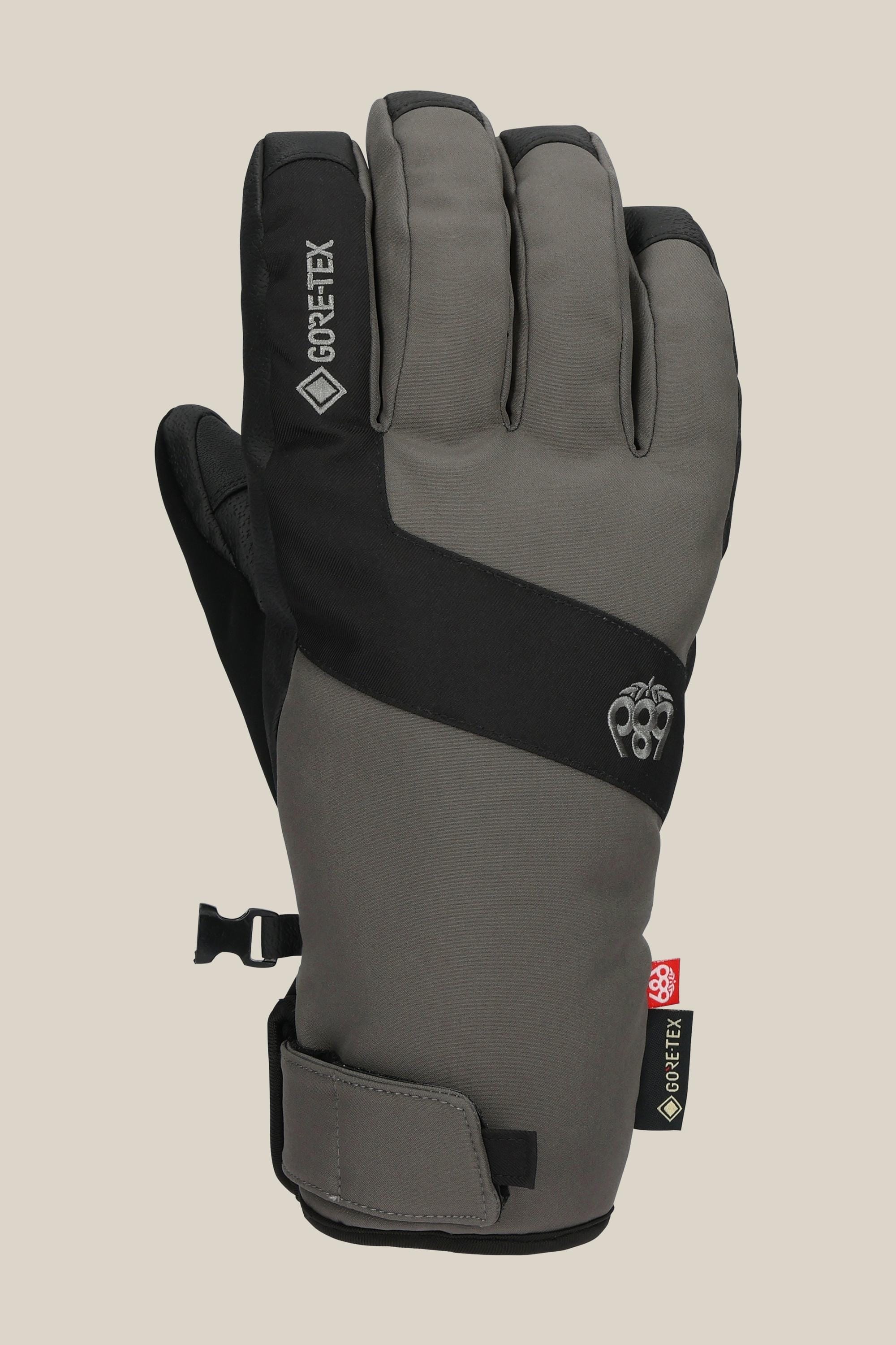 The 686 Mens GORE-TEX Linear Under Cuff Glove, shown in gray and black with small logos, a GORE-TEX tag, and an adjustable wrist strap, offers excellent winter protection and is photographed against a beige background.