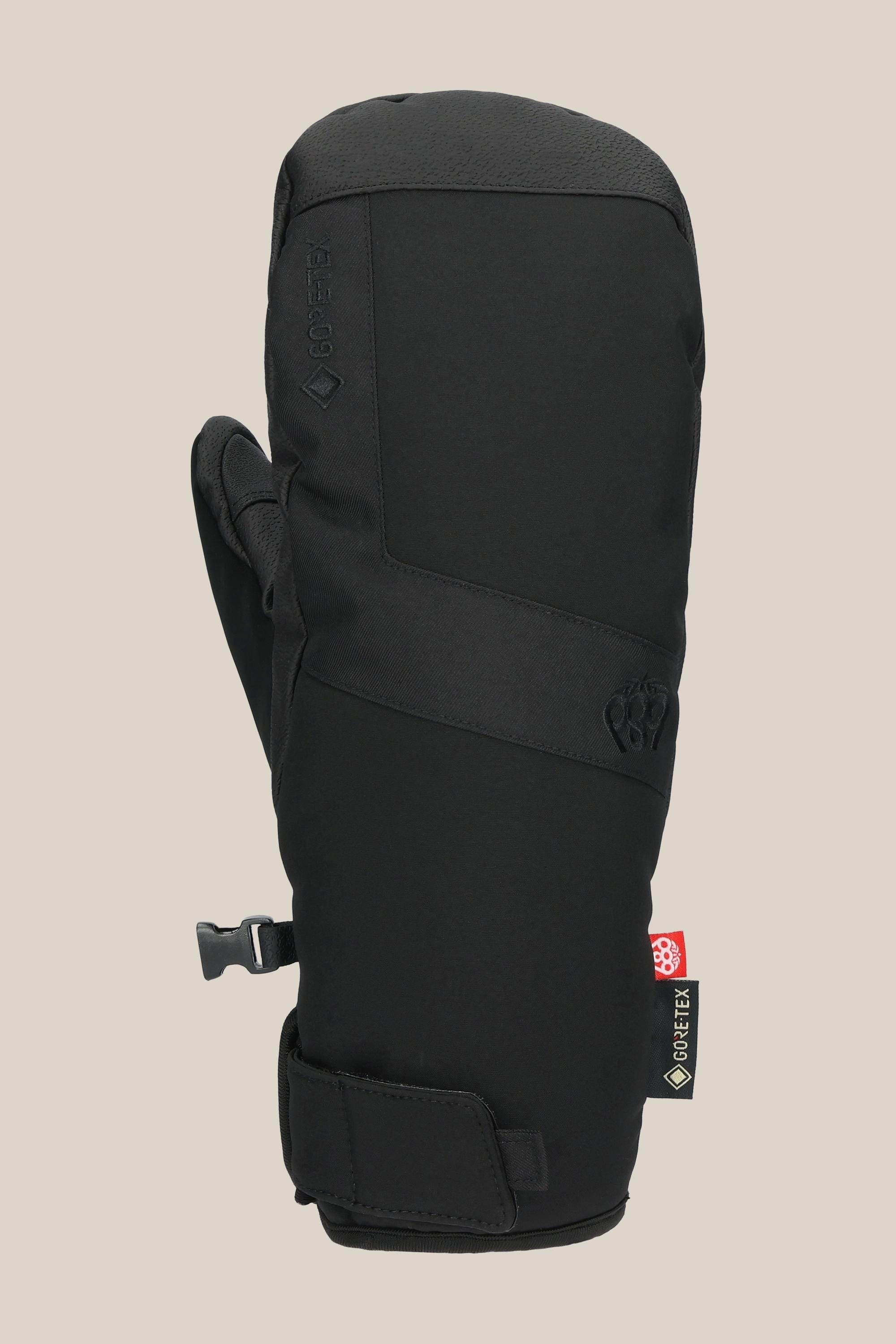 The 686 Mens GORE-TEX Linear Under Cuff Mitt features black insulation, a Velcro wrist strap, side buckle, and GORE-TEX tag—ideal as your winter go-to PU mitt. Displayed against a plain beige background.
