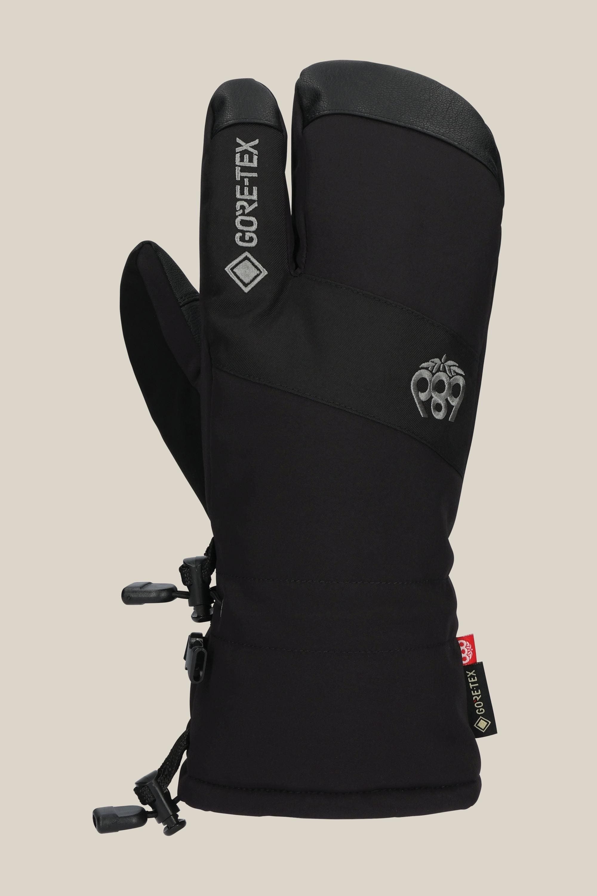 The 686 Men's GORE-TEX Linear Trigger Mitt, a black three-finger glove featuring adjustable wrist straps and a small embroidered logo on the back, by 686, is shown against a plain beige background.