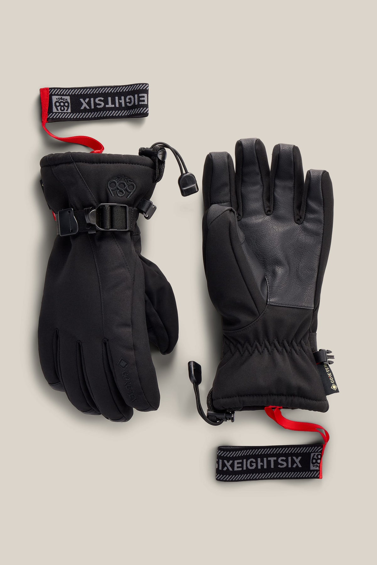 A pair of 686 Women’s GORE-TEX® Linear™ Gloves in black, featuring wrist straps and red pull tabs labeled “686.” One glove is shown with the palm side visible, while the other displays the back side with a buckle.