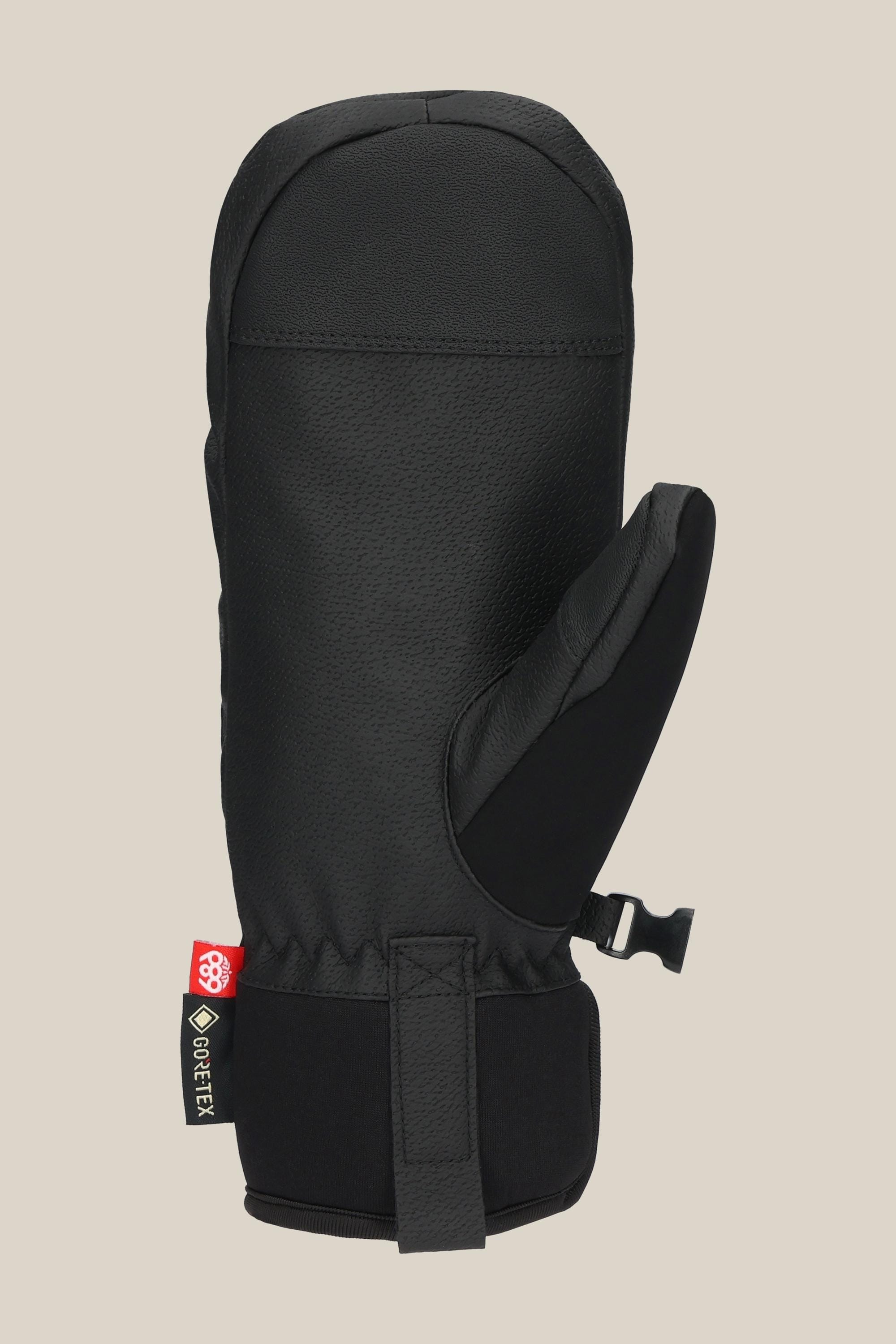 The 686 Womens GORE-TEX Linear Under Cuff Mitt by 686 is a black womens mitten made from poly with a textured PU surface, an adjustable wrist strap, and a small red GORE-TEX tag, shown on a plain beige background.