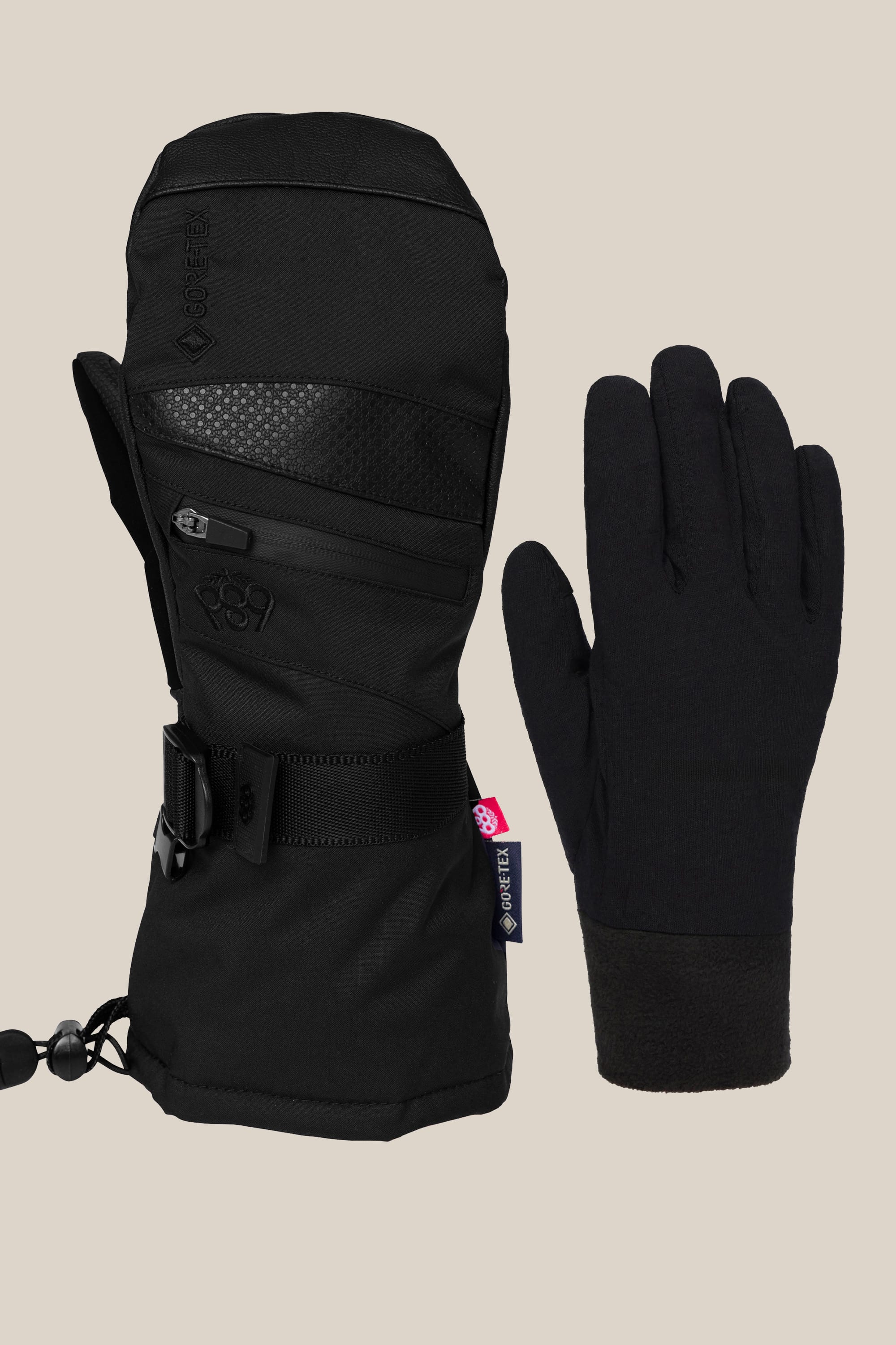 The 686 Womens GORE-TEX Smarty 3-In-1 Gauntlet Mitt by 686 features a bulky, insulated black mitt with a zipper and wrist strap alongside a slimmer five-finger liner glove, both shown on a plain beige background.
